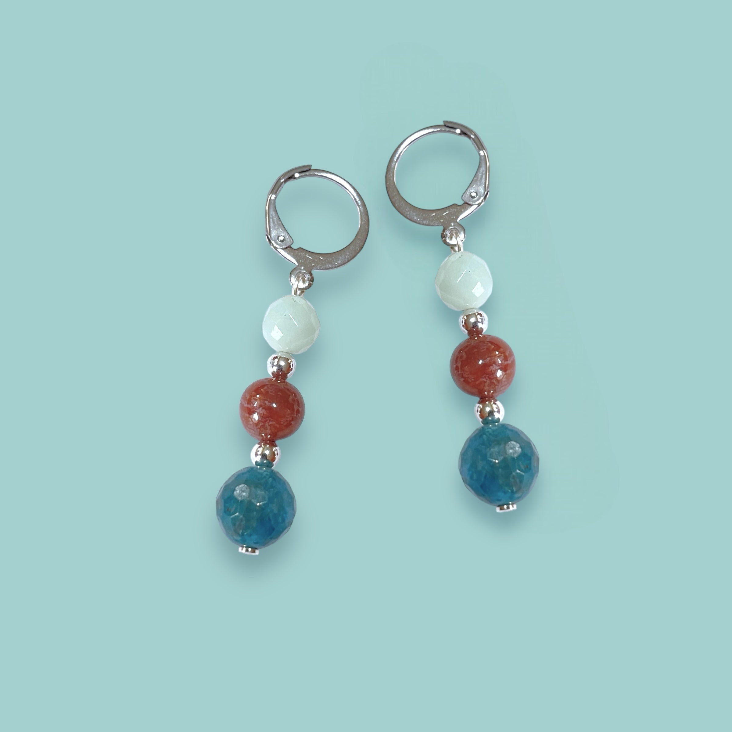 Boucles d'oreilles pendantes argentées en perles de pierres naturelles colorées dans les tons bleu et brique sur fond vert pastel