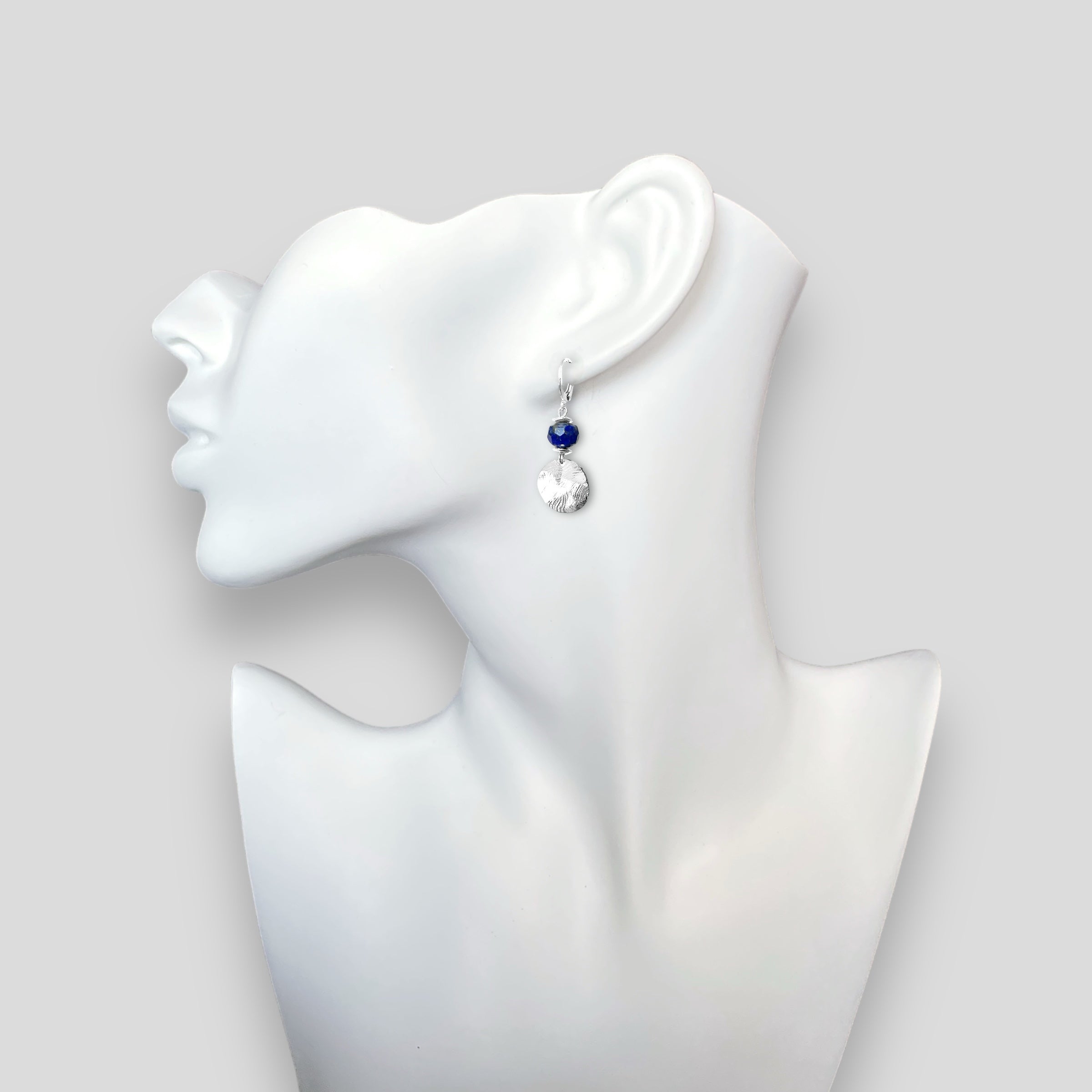 Petites boucles d'oreilles avec sequin rond en métal martelé argenté et perles de Lapis Lazuli, portées à l'oreille sur un buste blanc