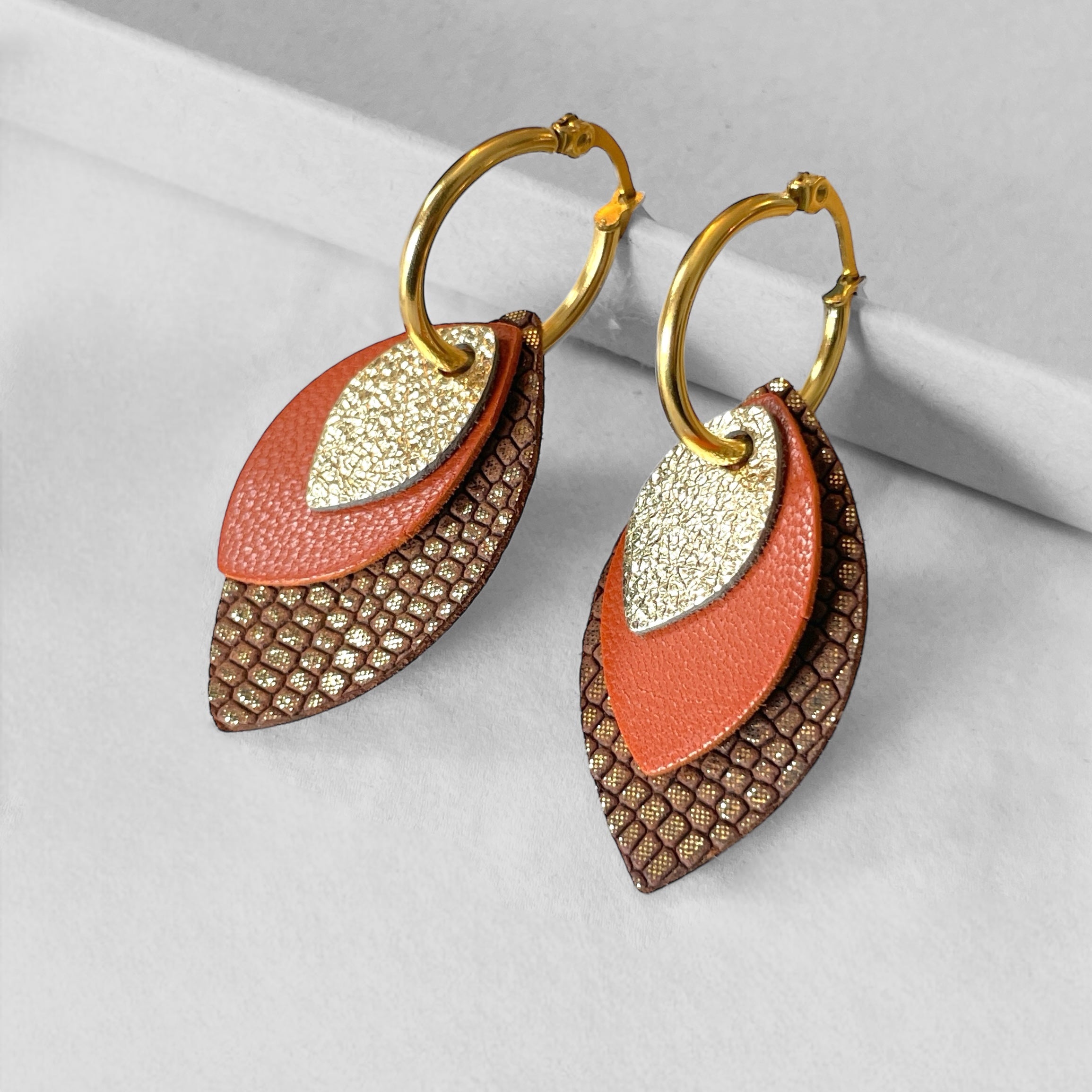 Créoles dorées avec pendentifs modulables en forme de feuilles en cuirs doré antique, camel et taupe or façon serpent, sur fond gris