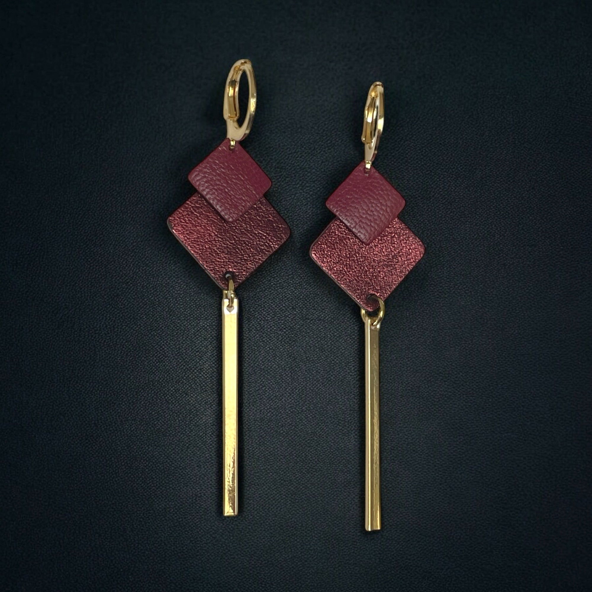 boucles d'oreilles dorées Nune modèle Ada avec duo de losanges en cuirs pourpre et grenat métallisé et longue tige fine dorée sur fond blanc
