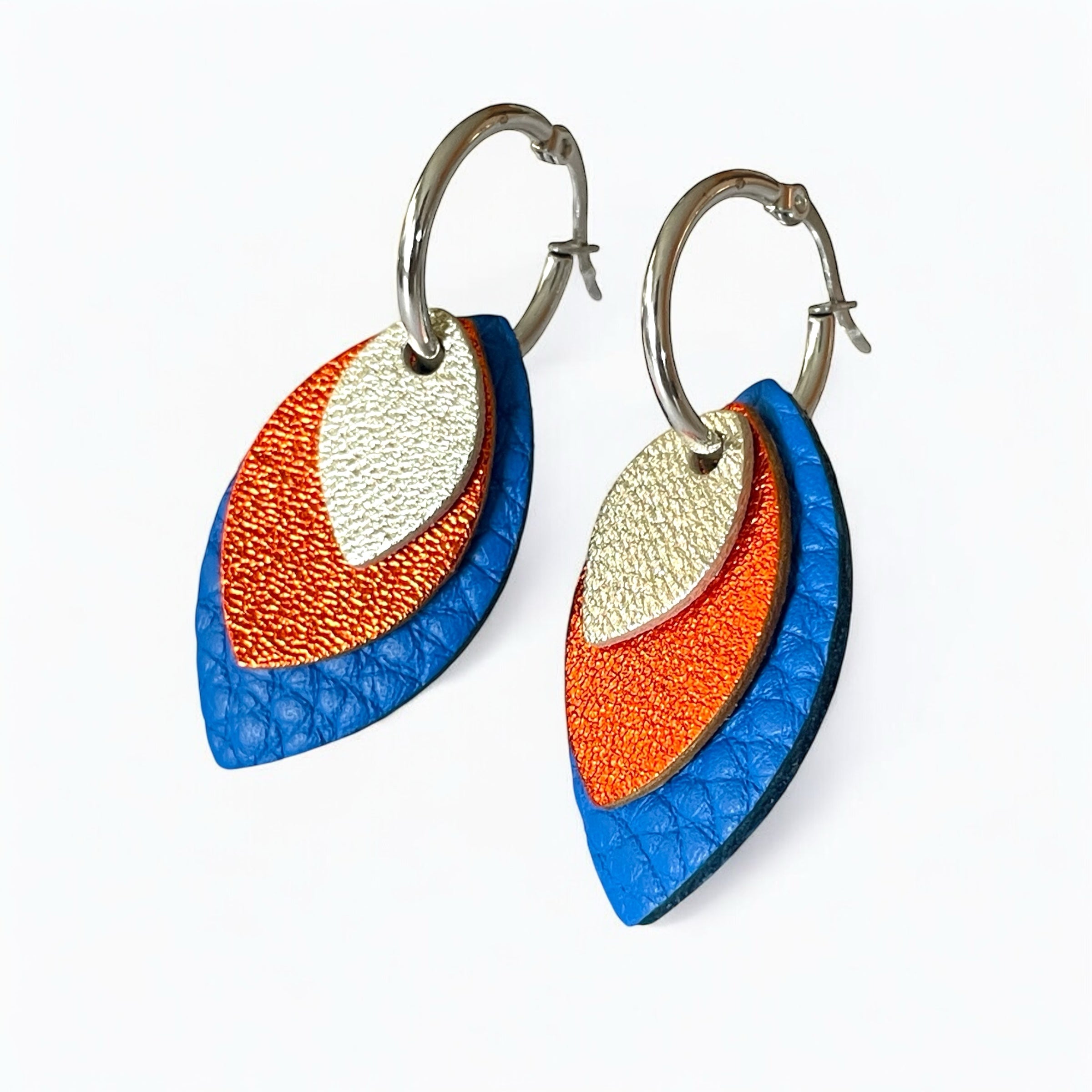 Créoles argentées avec pendentifs modulables en forme de feuilles en cuirs argent, orange sanguine métallisé et bleu roi grainé, sur fond blanc