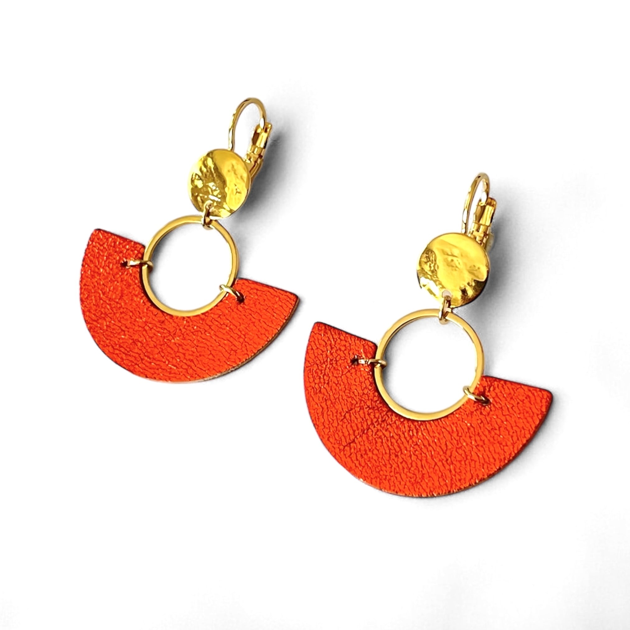 paire de boucles d'oreilles dorées pendantes en forme de demi-lunes en cuir orange sanguine métallisé, sur fond blanc