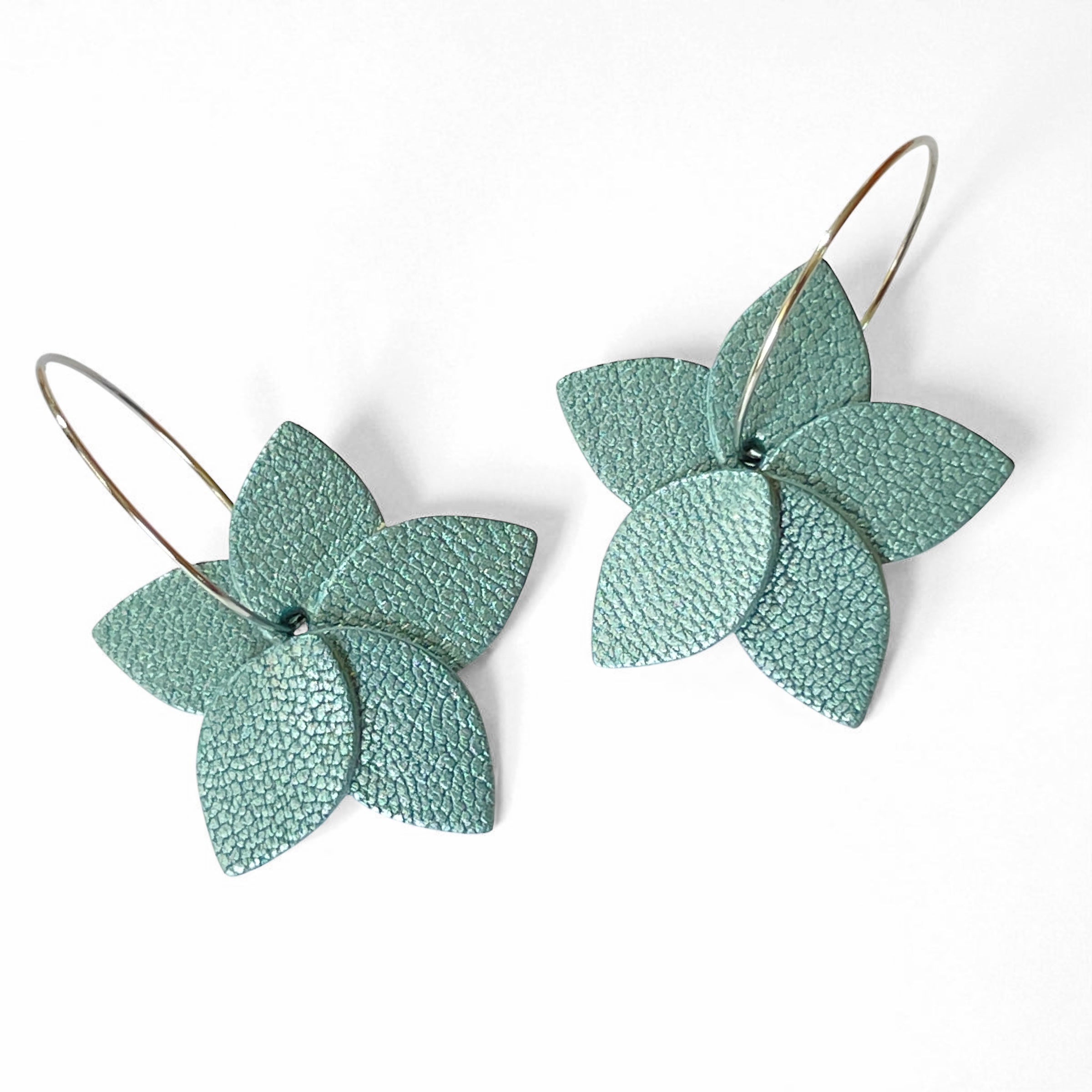 Petites boucles d'oreilles en forme de fleurs en cuir bleu gris nacré, montées sur créoles argentées, sur fond blanc