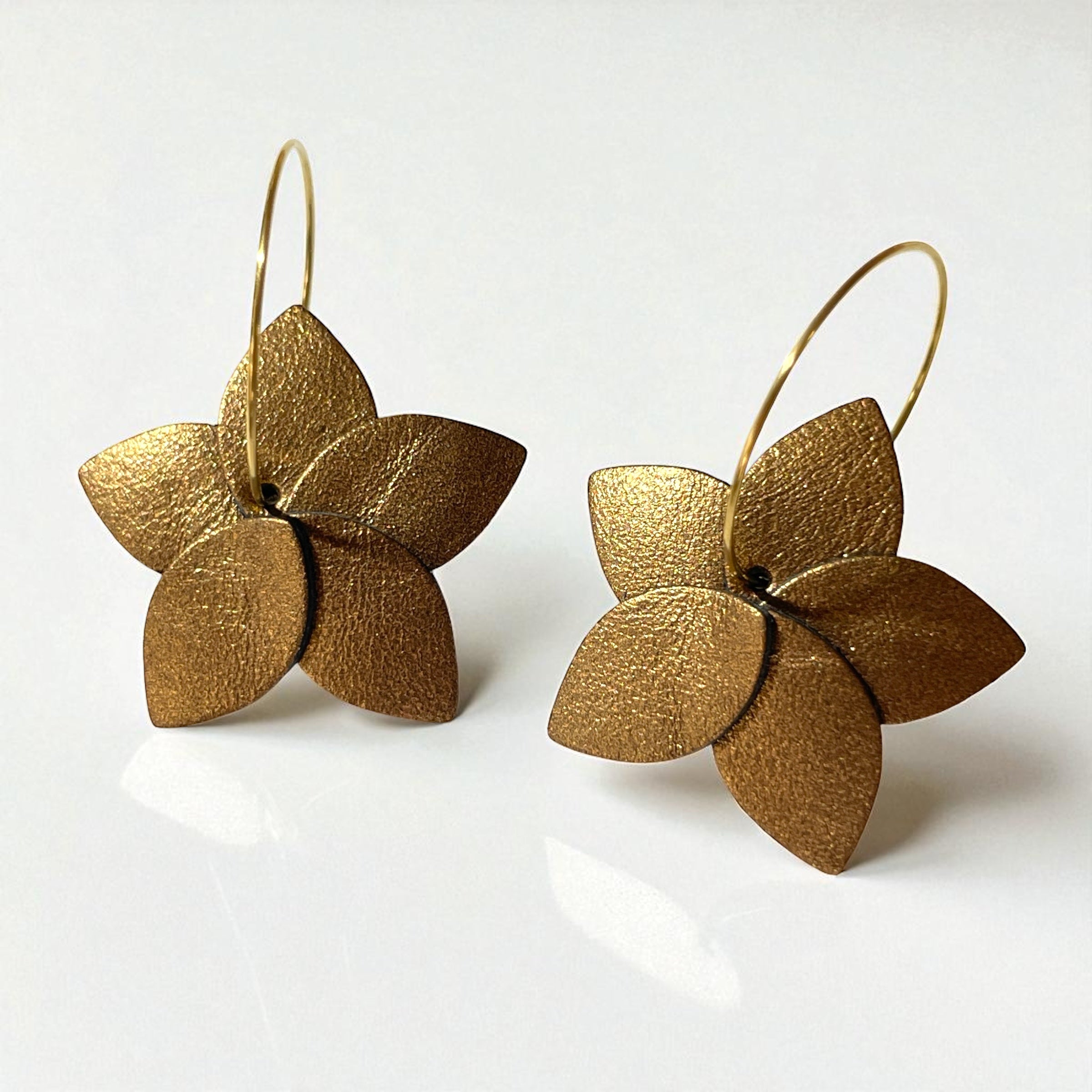 Petites boucles d'oreilles en forme de fleurs en cuir bronze métallisé, montées sur créoles dorées, sur fond blanc