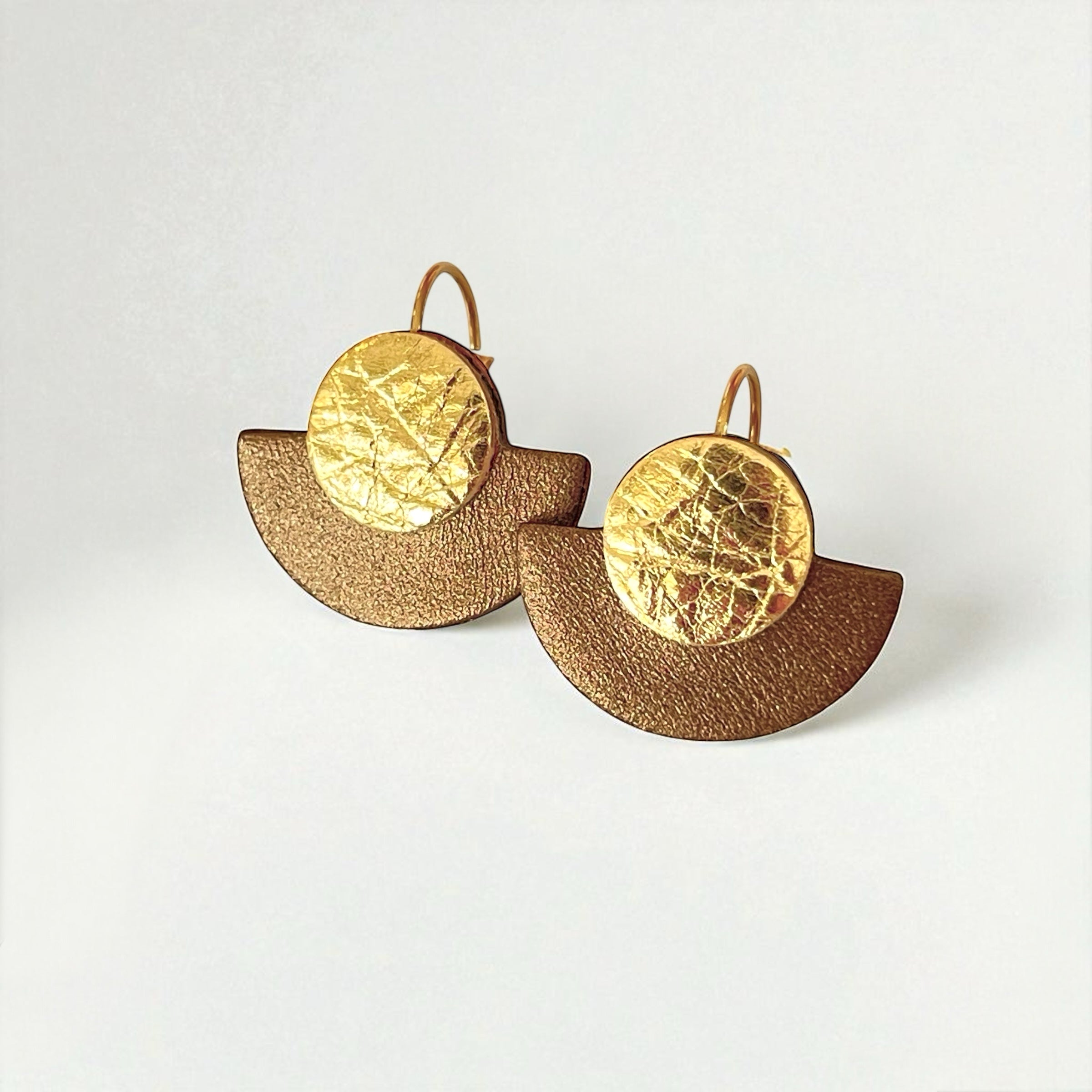 boucles d'oreilles dorées en forme de demi-lunes en cuirs doré et bronze métallisé, sur fond blanc