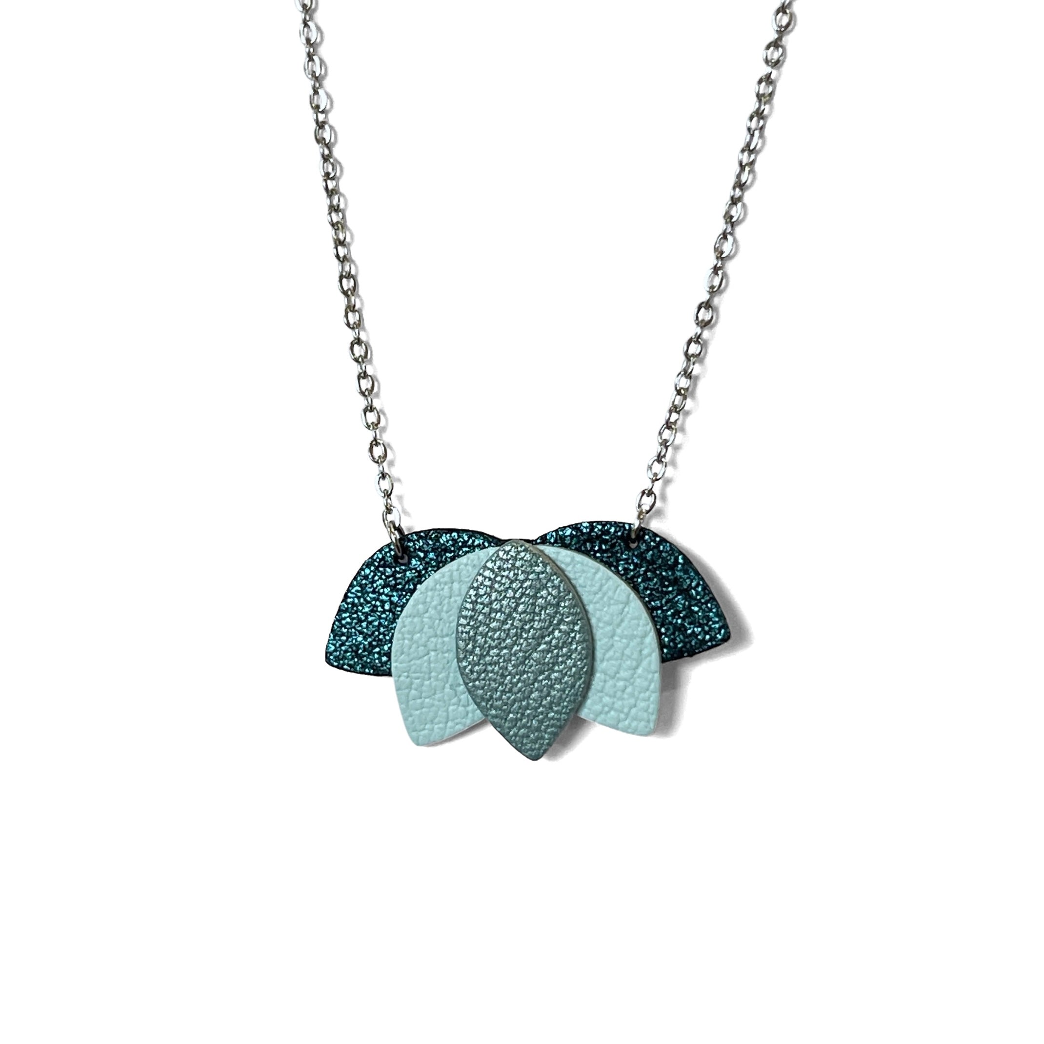 Collier argenté court et délicat avec un pendentif en forme de Lotus, composé de cuirs bleu paon pailleté, bleu nuage et bleu gris nacré, sur fond blanc