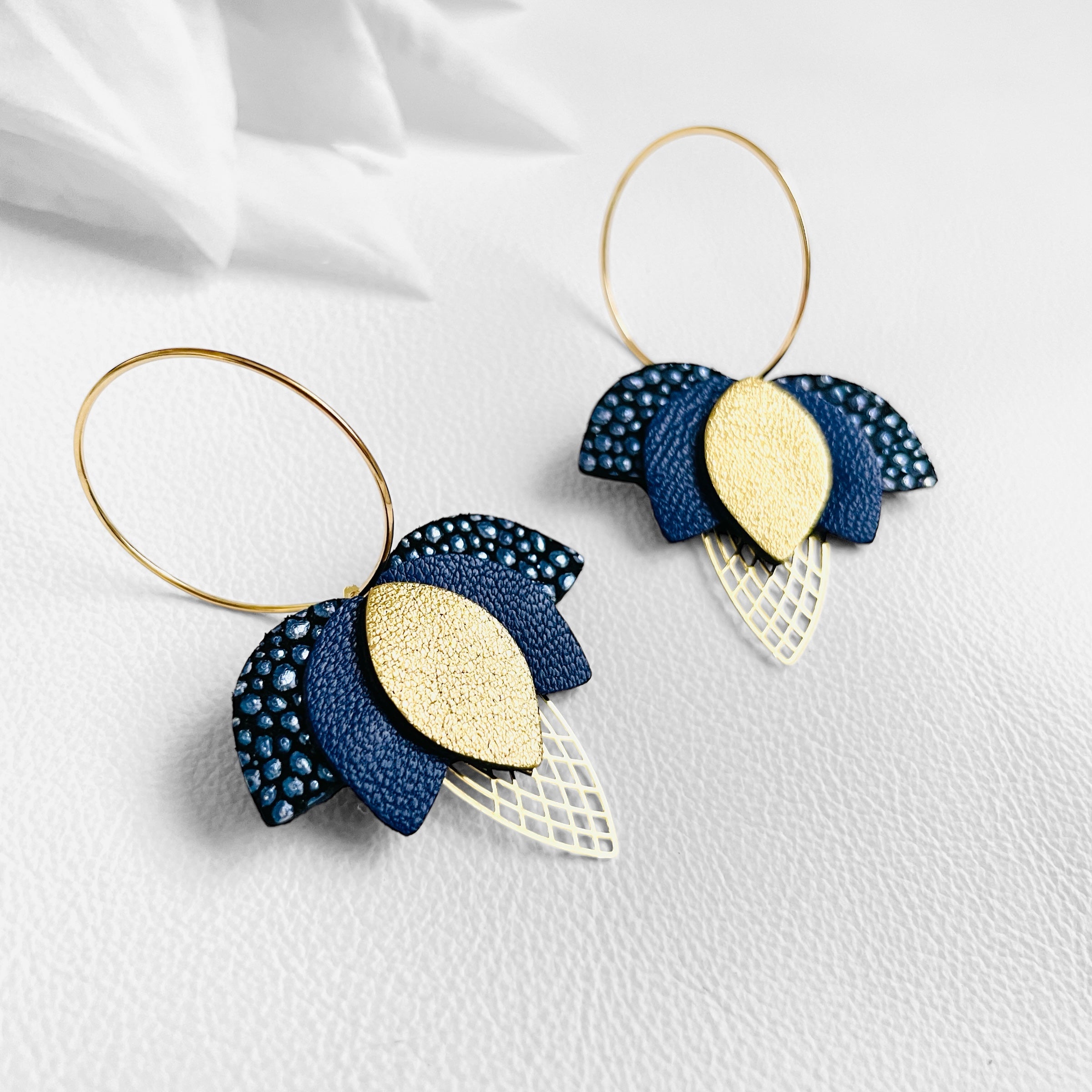 Créoles dorées en forme de fleurs de Lotus en cuirs bleu nuit grainé métallisé, bleu nuit et doré satiné sur fond blanc