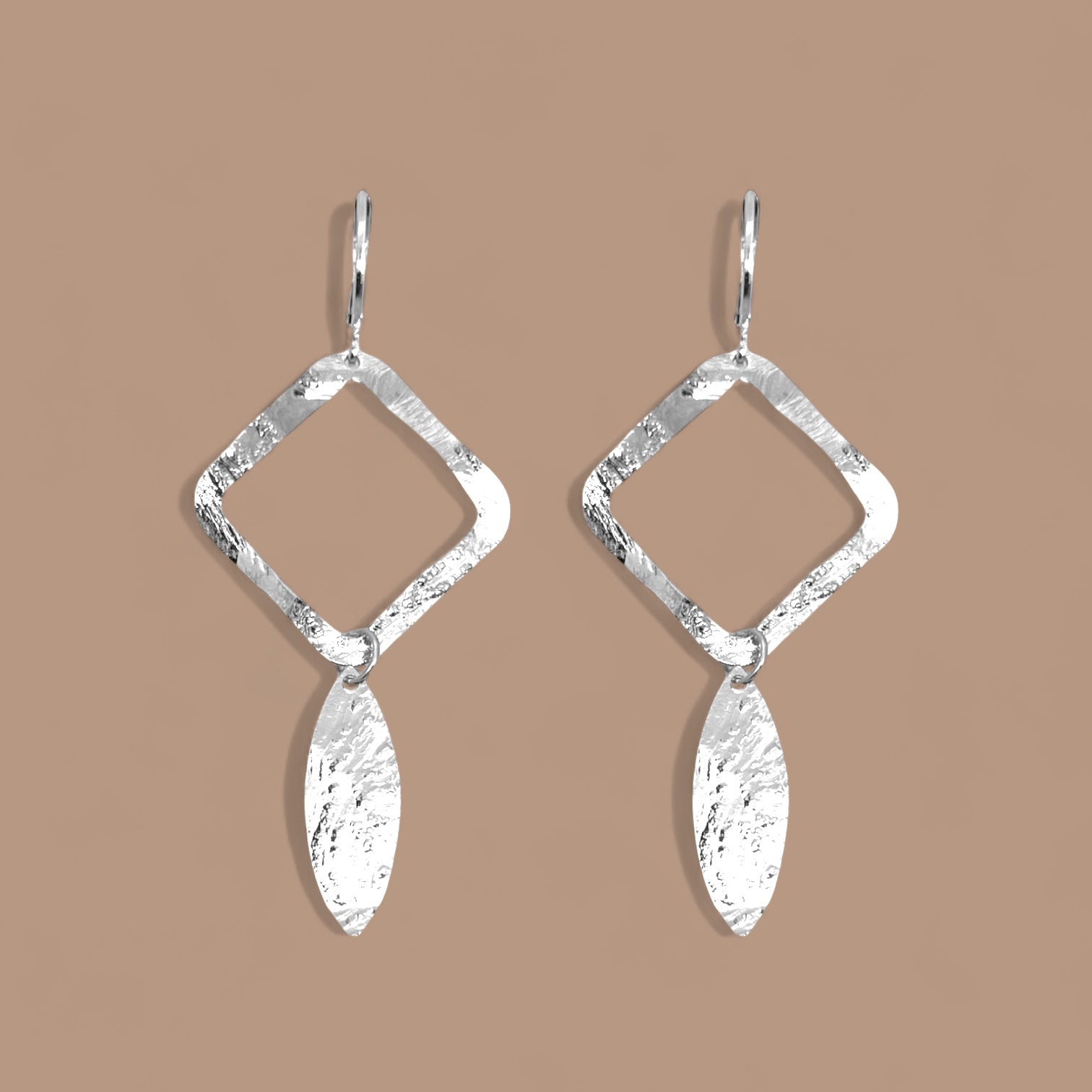 Boucles d'oreilles argentées avec pendentif en forme de losanges et pointes, sur fond beige