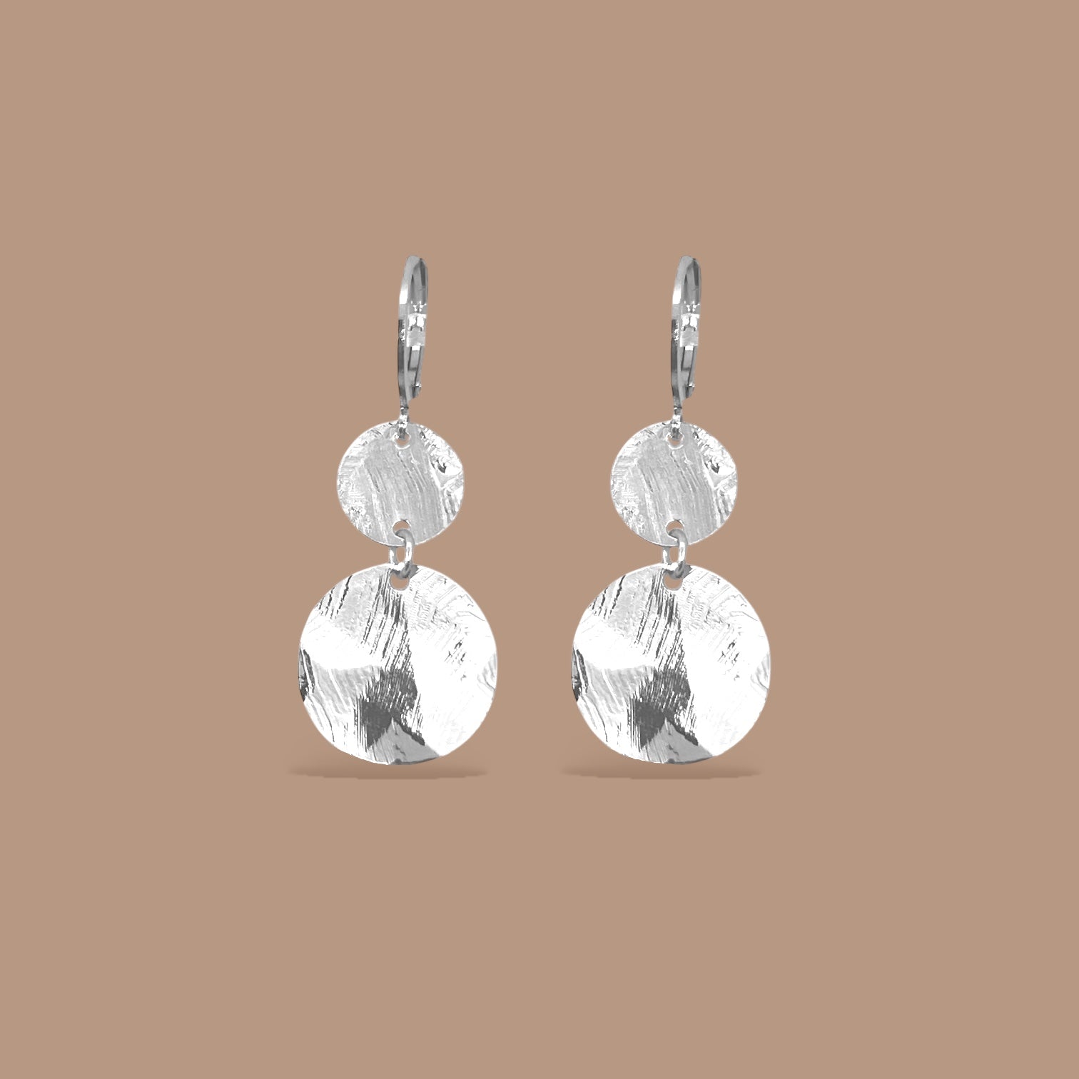 Petites boucles d'oreilles argentées pendantes avec 2 petits sequins ronds en métal martelé, sur fond beige