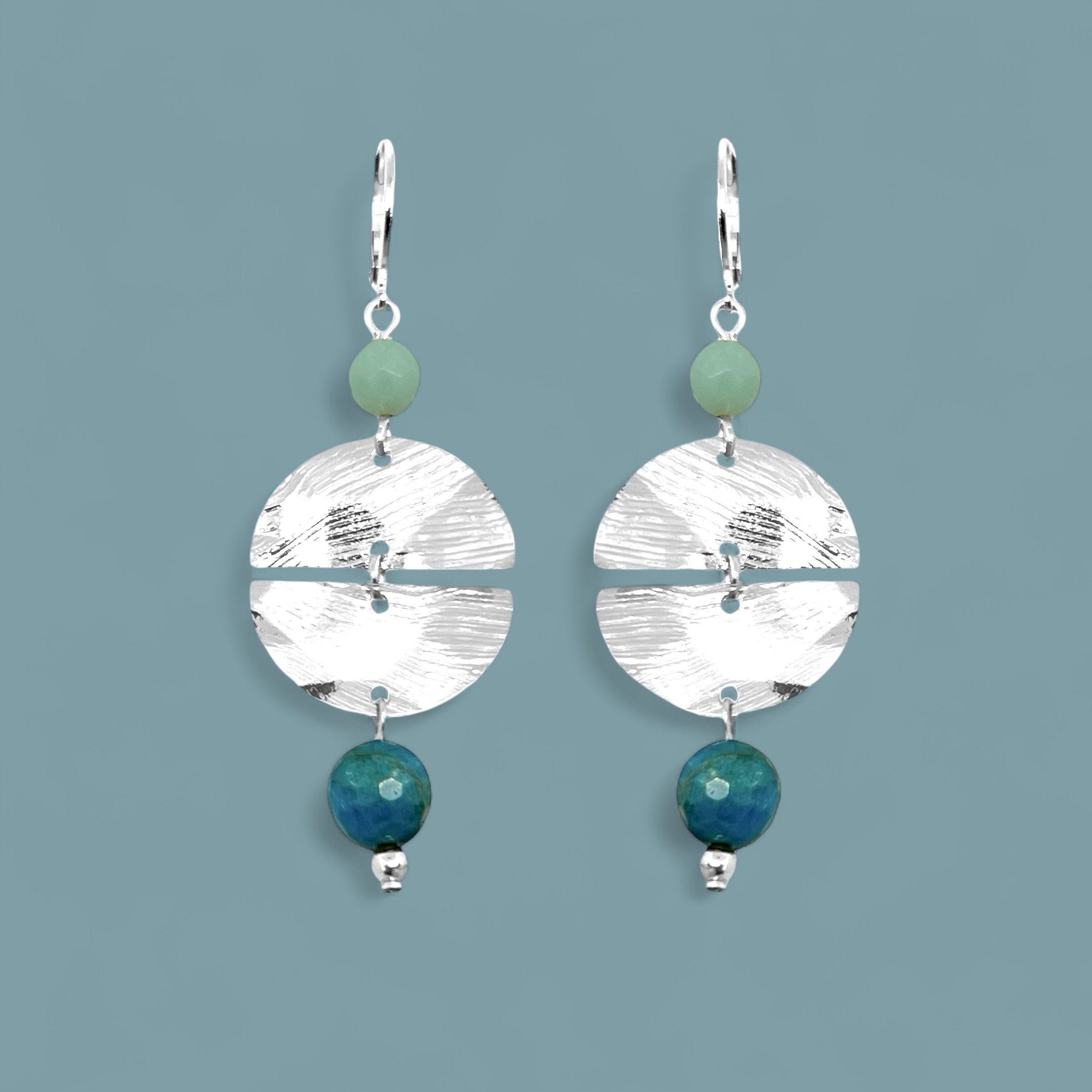 Boucles d'oreilles pendantes de forme ronde avec 2 demi-lunes, en métal martelé argenté et perles d'amazonite et d'apatite bleue, sur fond bleu gris
