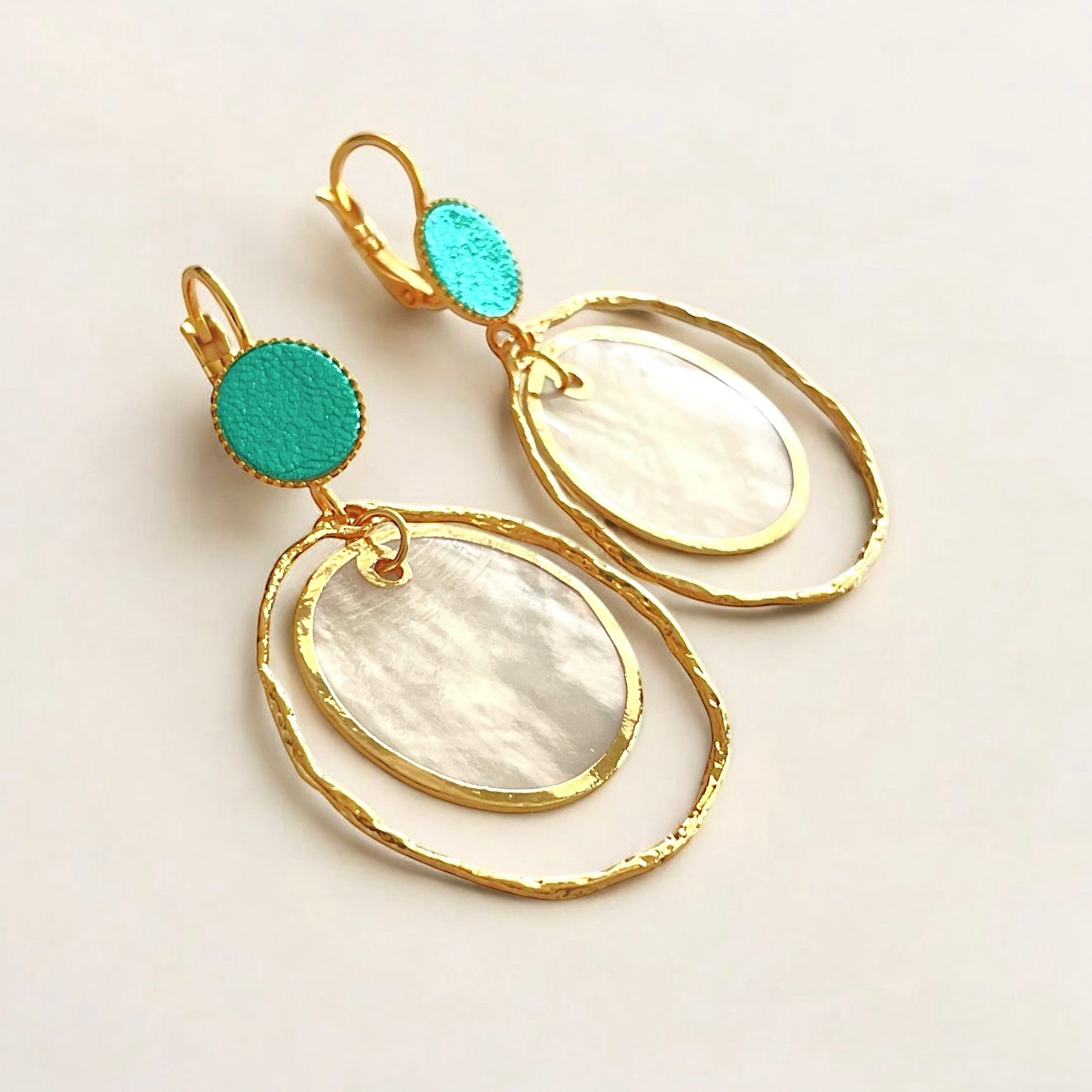 boucles d'oreilles dorées Nune modèle Bali Créoles Capiz en cuir turquoise métallisé sur fond beige