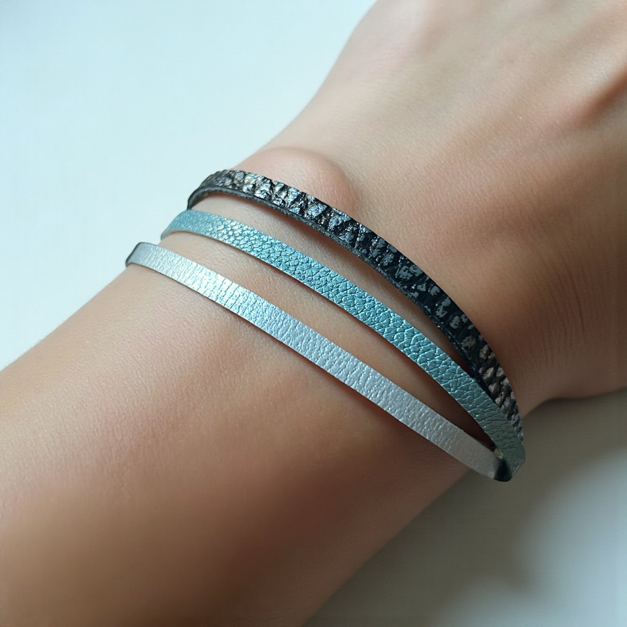 Cielo Bracelet femme tricolore à 3 liens avec fermoir aimanté doré, en cuirs bleu gris nacré, bleu glacier métallisé grainé, et champagne nacré, porté au poignet, sur fond blanc