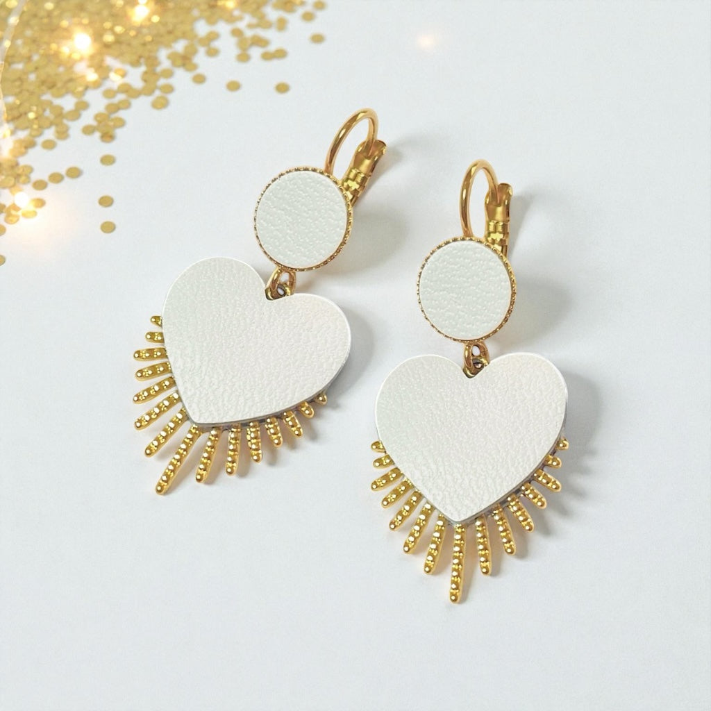 NUNE Boucles d'oreilles dorées Vénus en forme de cœurs style ex-voto en cuir blanc satiné sur fond blanc parsemé de paillettes dorées