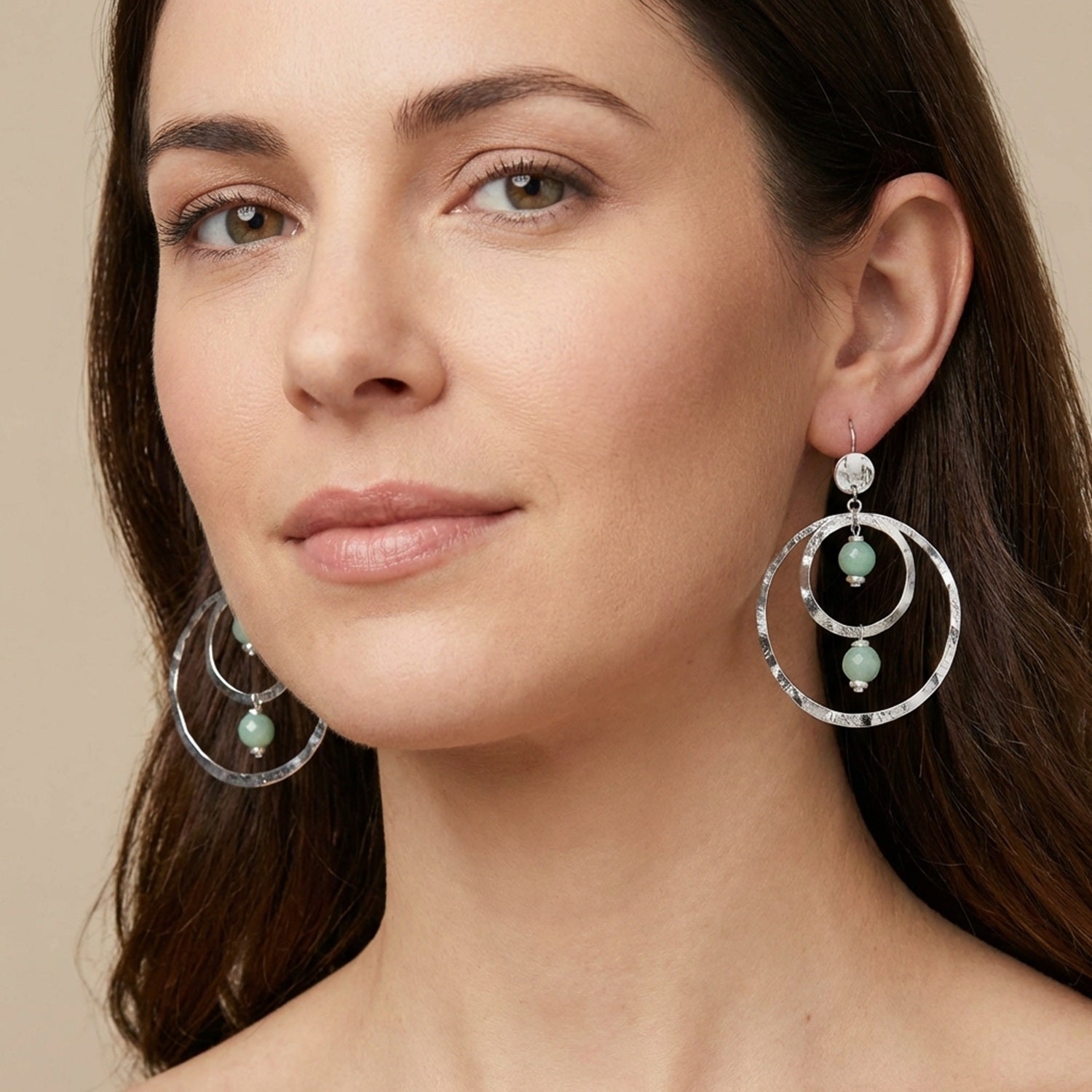 Grandes boucles d'oreilles créoles en métal martelé argenté et perles minérales naturelles d'amazonite, de forme ronde, avec doubles anneaux, portées aux oreilles par une femme brune