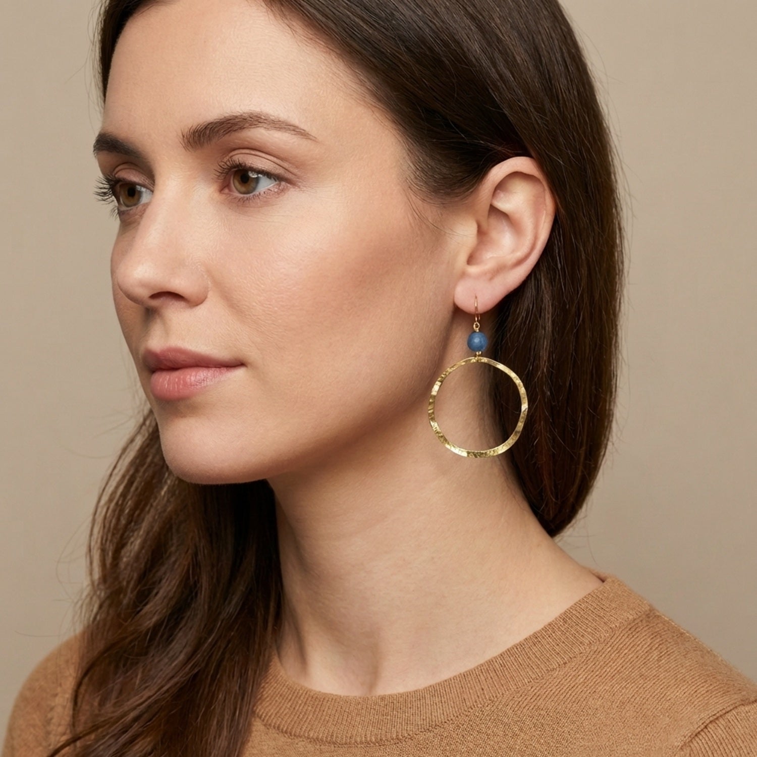 Boucles d'oreilles créoles de forme ronde en métal martelé doré à l'or fin et perles d'aventurine, portées à l'oreille par une femme brune