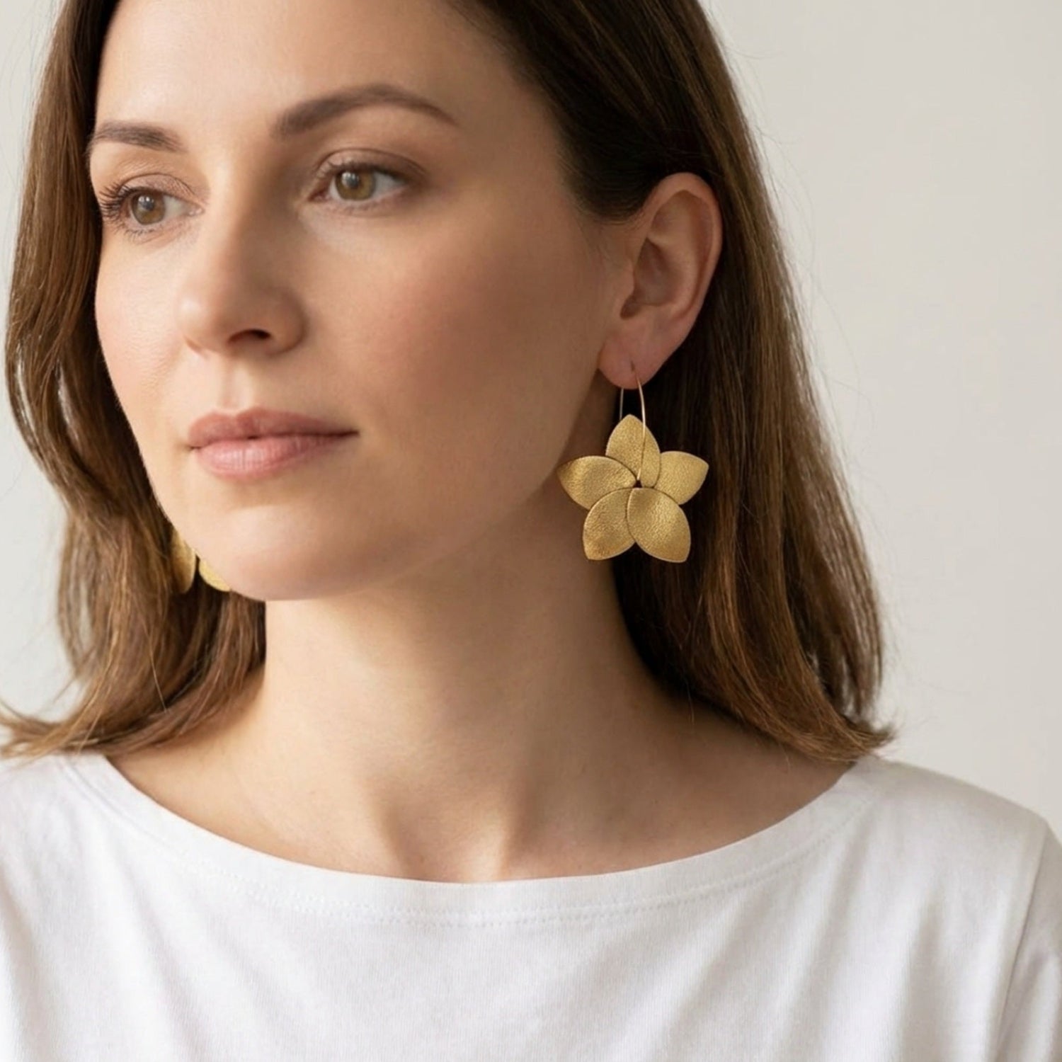 Boucles d'oreilles créoles Tiara de Nuneen forme de grosse fleur en cuir doré satiné et anneaux dorés, portées à l'oreille