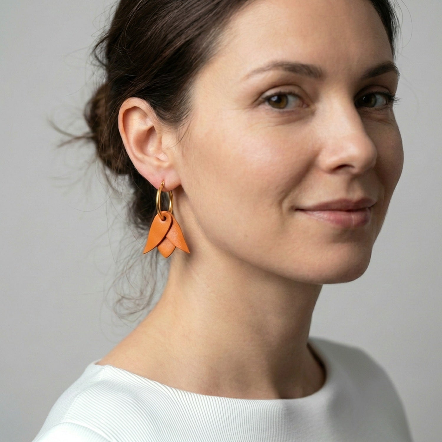 Boucles d'oreilles créoles dorées avec pendentifs légers en cuir orange mandarine en forme de tulipe, portées aux oreilles