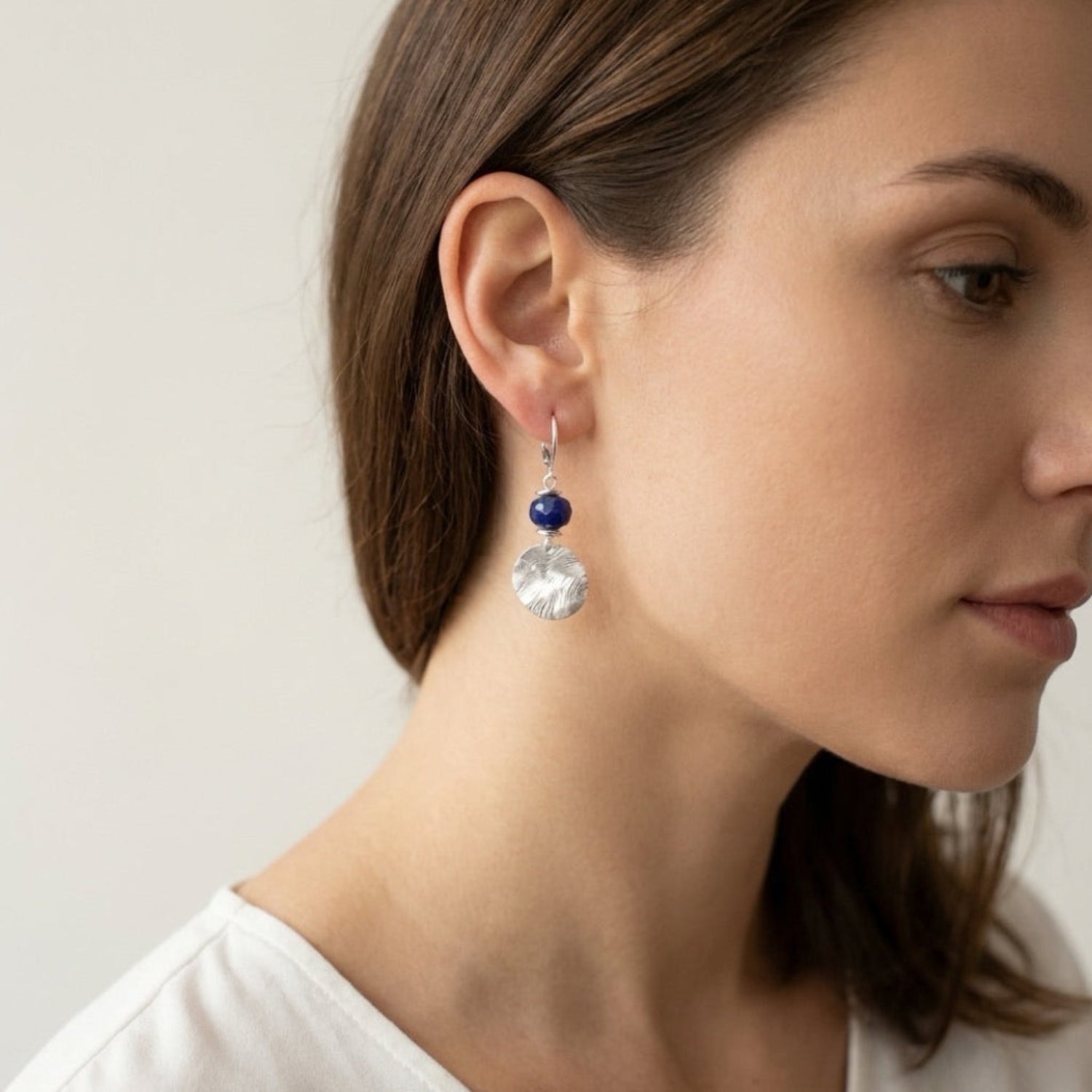 Petites boucles d'oreilles avec sequin rond en métal martelé argenté et perles de Lapis Lazuli, portées à l'oreille
