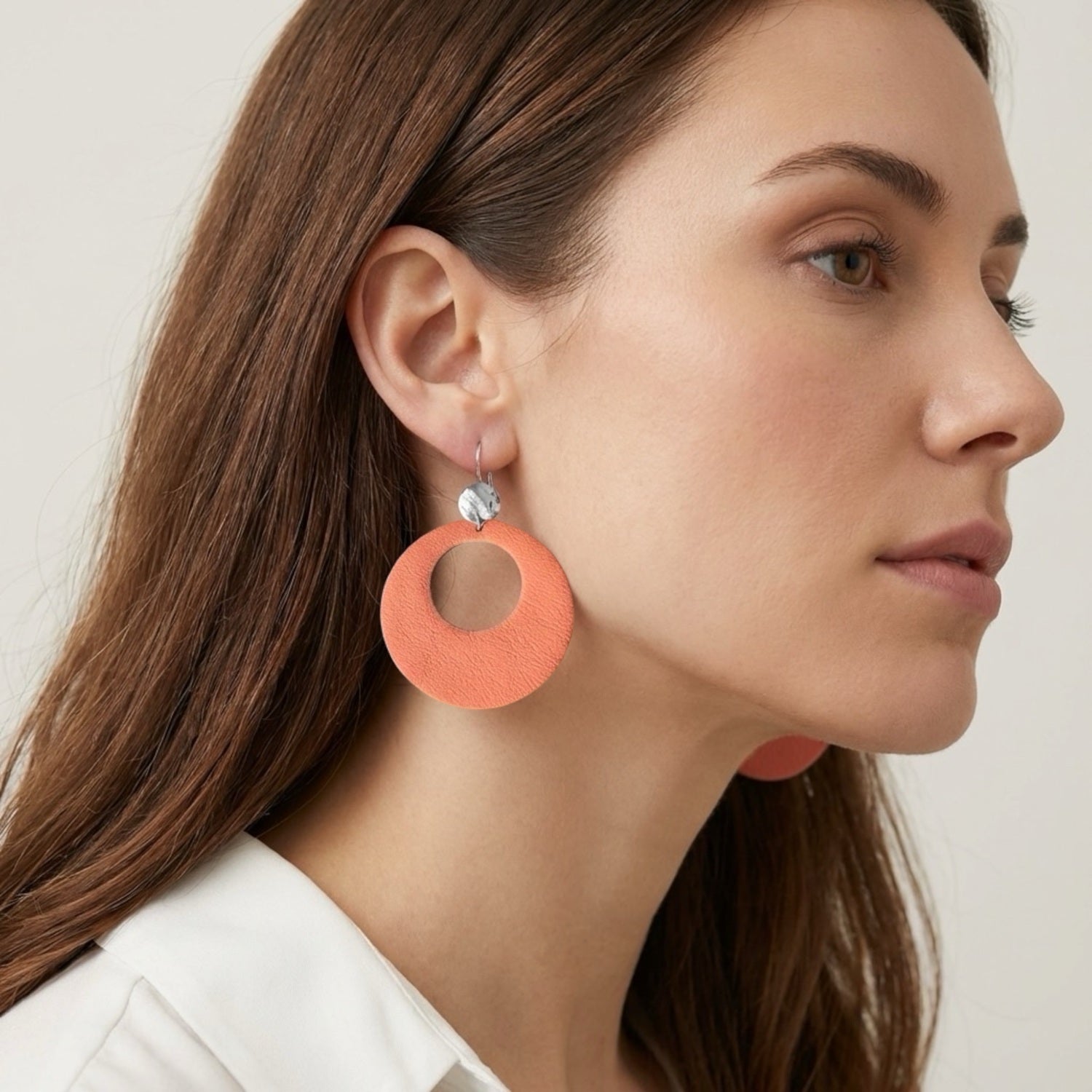 Boucles d'oreilles argentées, grandes créoles rondes en cuir saumon clair au style vintage, portées aux oreilles par une femme brune