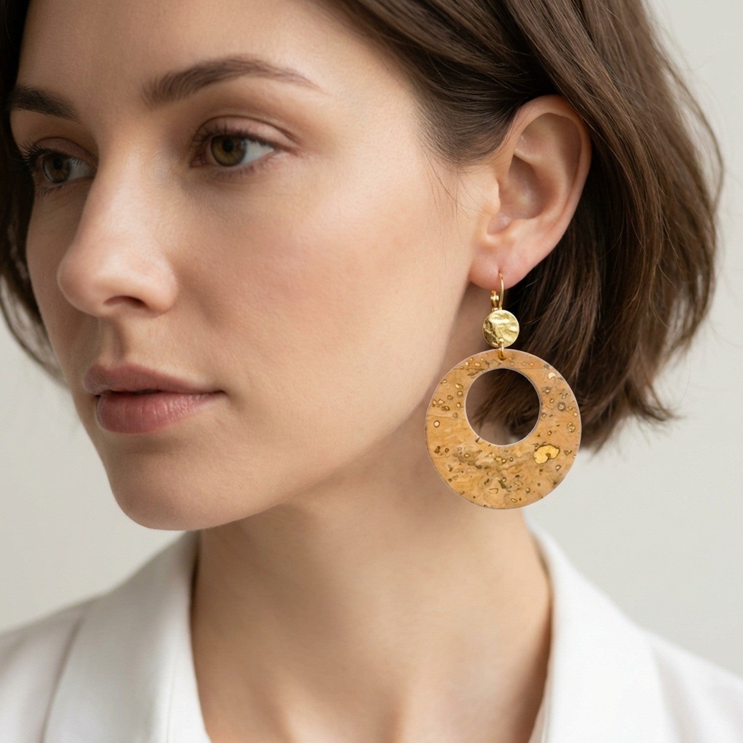 Femme brune portant des grandes boucles d'oreilles créoles Zoa rondes au style vintage en liège doré antique