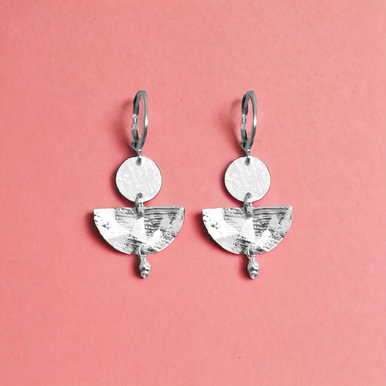 Petites boucles d'oreilles argentées pendantes en forme de demi-lunes, sur fond vieux rose