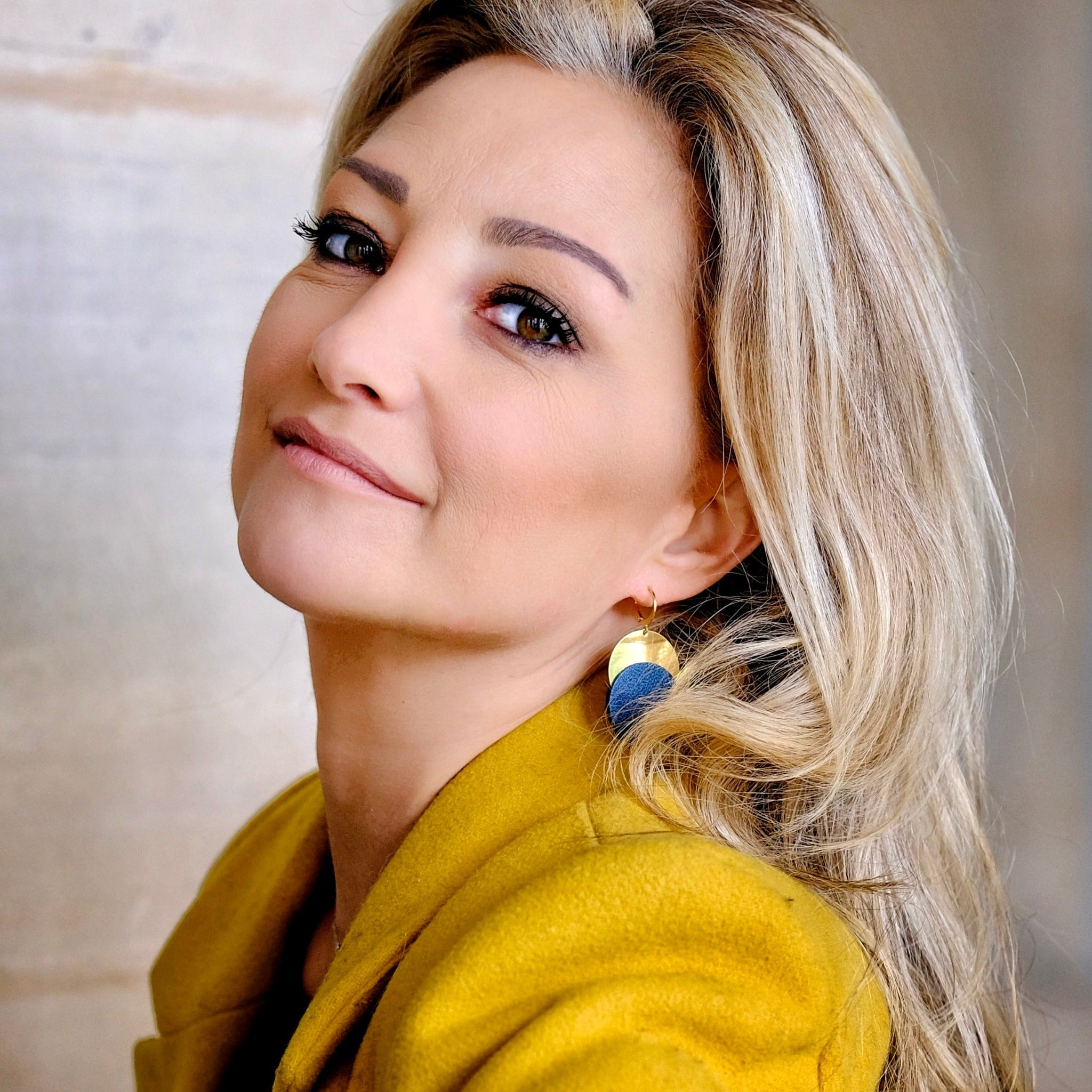 Femme blonde portant les Boucles d'oreilles dorées Nune modèle Eclipse avec disque de cuir bleu nuit sur un disque doré