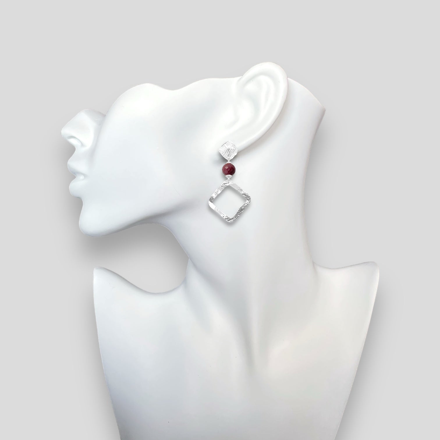Boucles d'oreilles losanges sur puces en métal martelé argenté et perles de Mokaïte bordeaux, portées à l'oreille sur un buste blanc