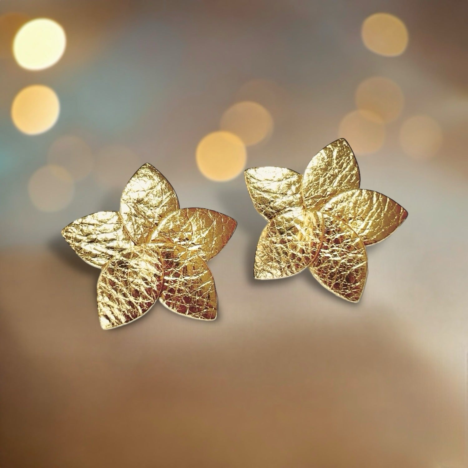 Paire de Boucles d'oreilles puces en forme de fleurs en pétales de cuir doré, sur fond beige lumineux