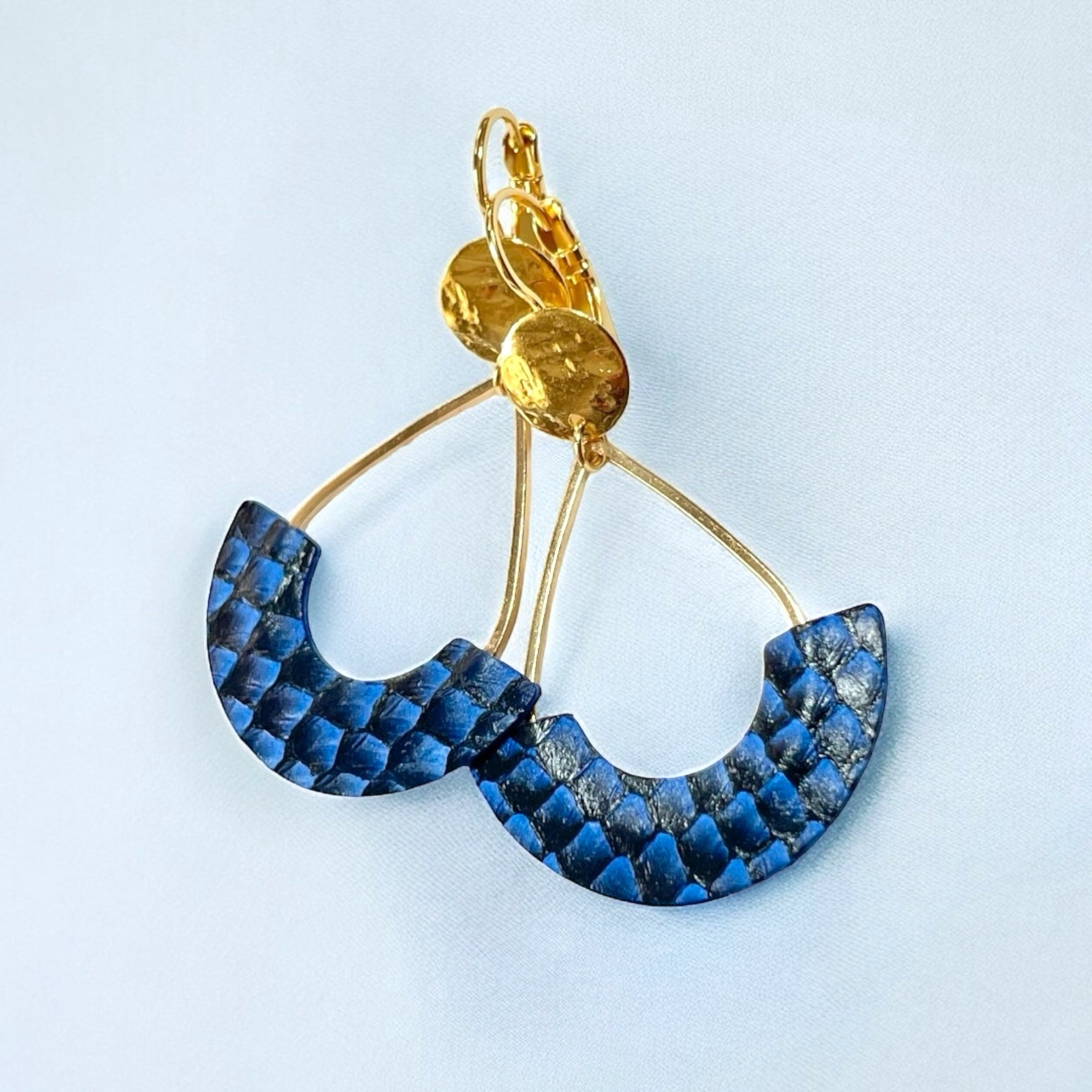 Boucles d'oreilles Anoush de Nune, dorées à l'or fin avec cuir marin, cuir de poisson saumon bleu saphir écaille, en forme de demi-lune, sur fond gris