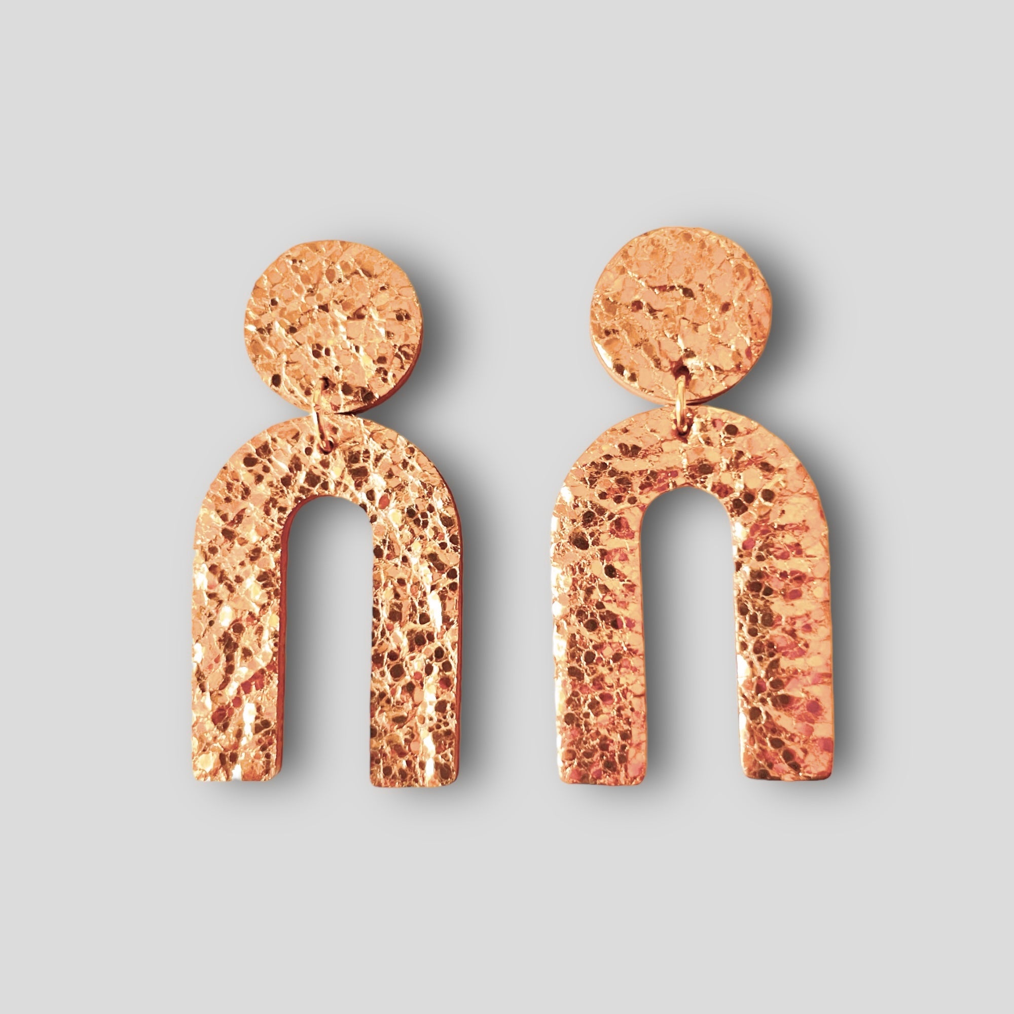 Puces d'oreilles Arkus marque Nune, en forme d'arches tout cuir or rosé froissé, sur fond gris