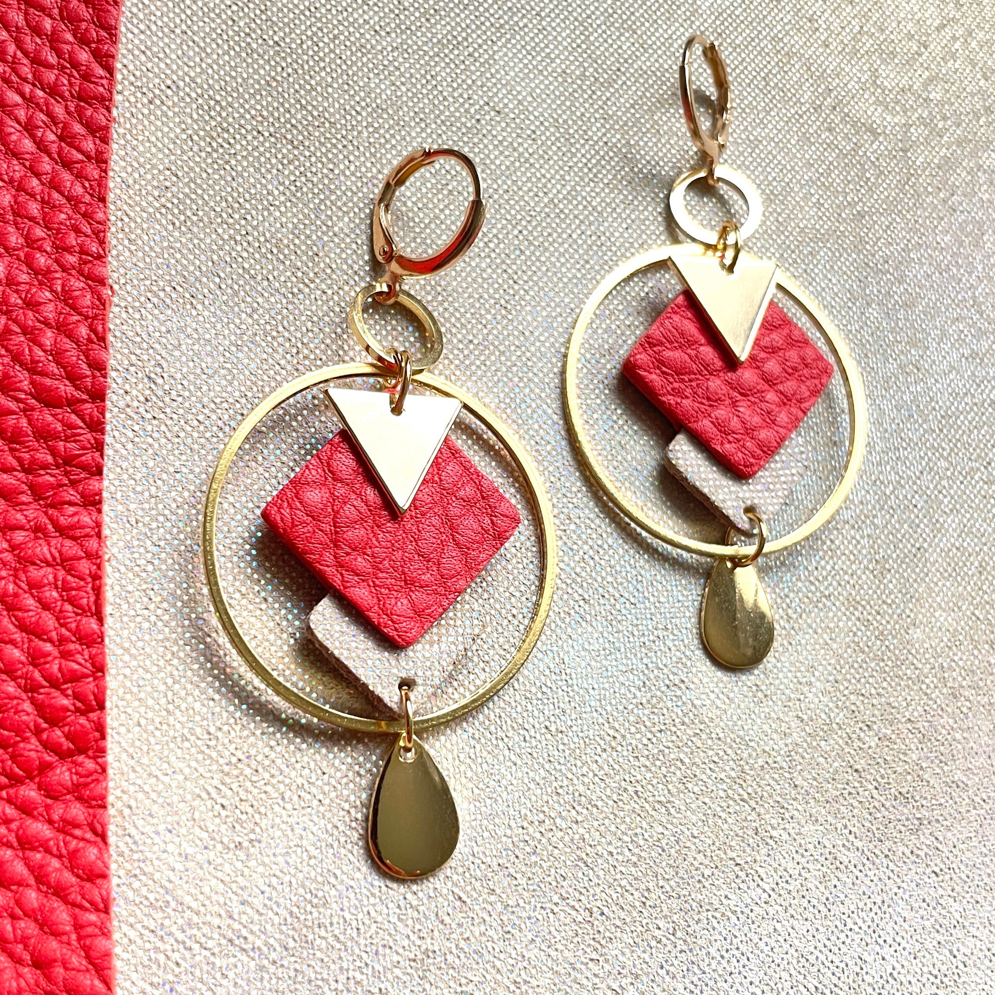 Boucles d'oreilles Nune modèle Créoles Adamante Or en cuir rouge vermillon grainé et laiton doré à l'or fin sur fond beige irisé
