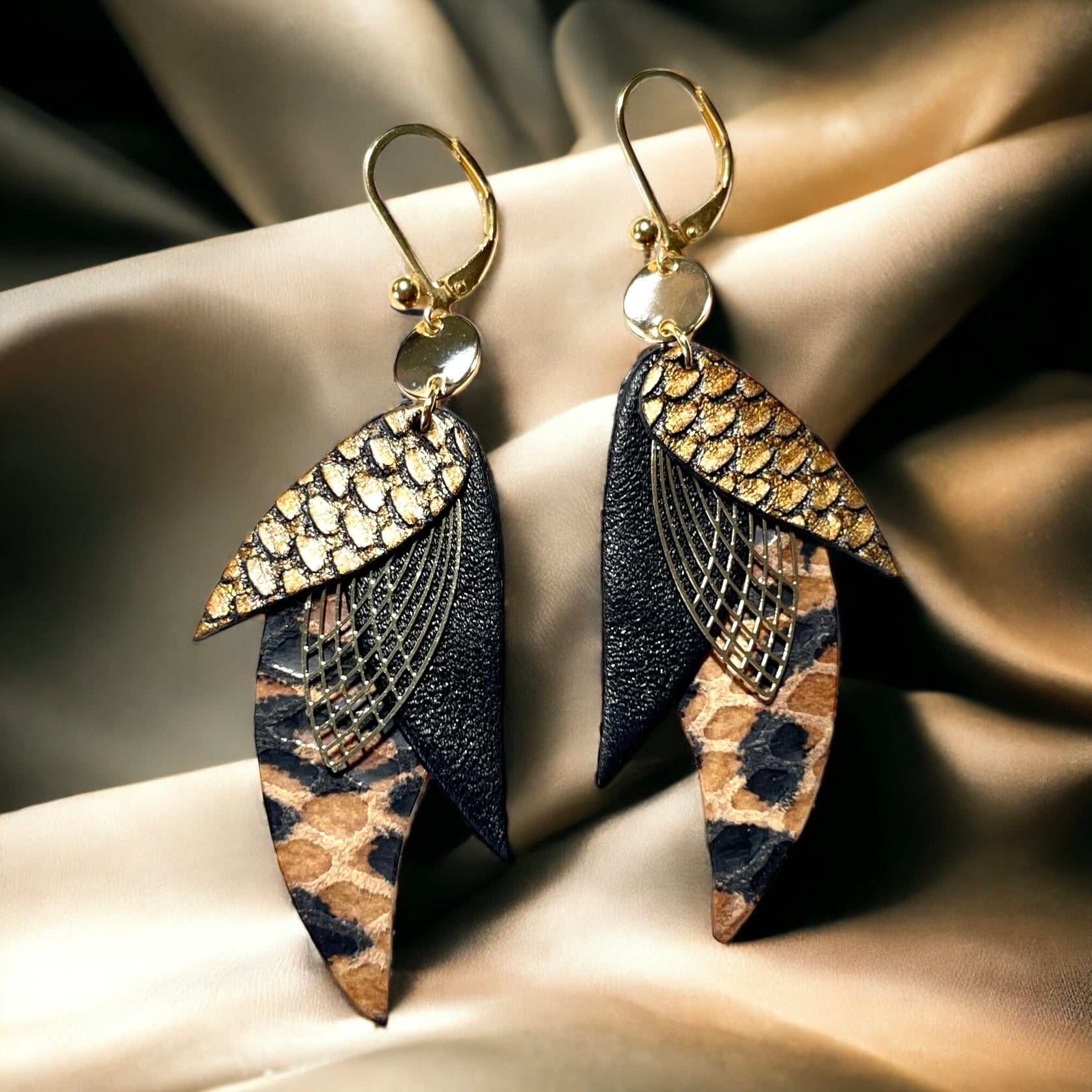 boucles d'oreilles dorées Nune modèle Ara en plumes de cuir bronze écaille patiné, noir satiné et façon léopard, sur un satin beige