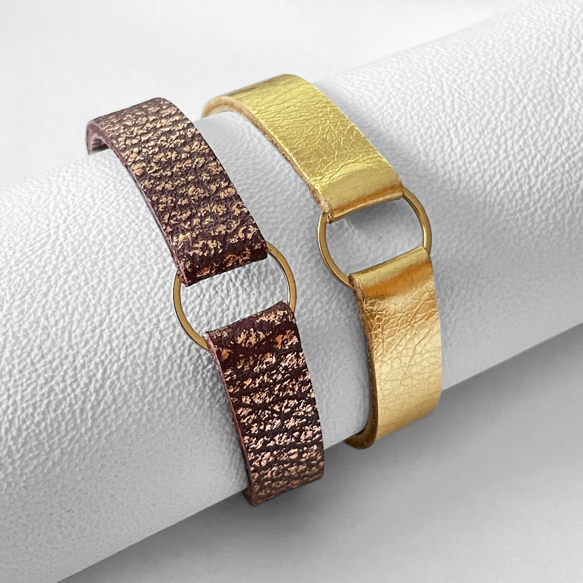 2 Bracelets en cuirs doré brillant et chocolat grainé ou rose avec fine boucle dorée, enroulés autour d'un rouleau de cuir blanc