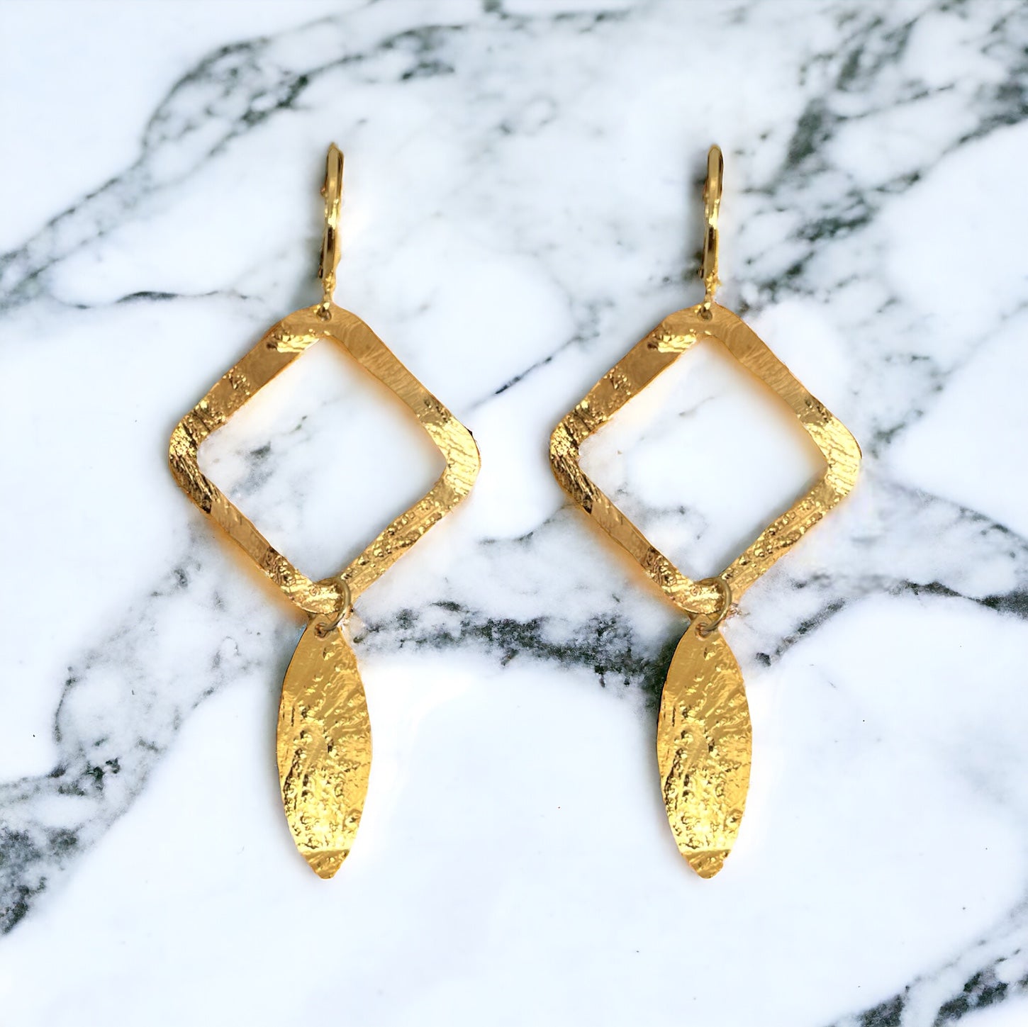 Boucles d'oreilles dorées avec pendentif en forme de losanges et pointes, sur marbre blanc