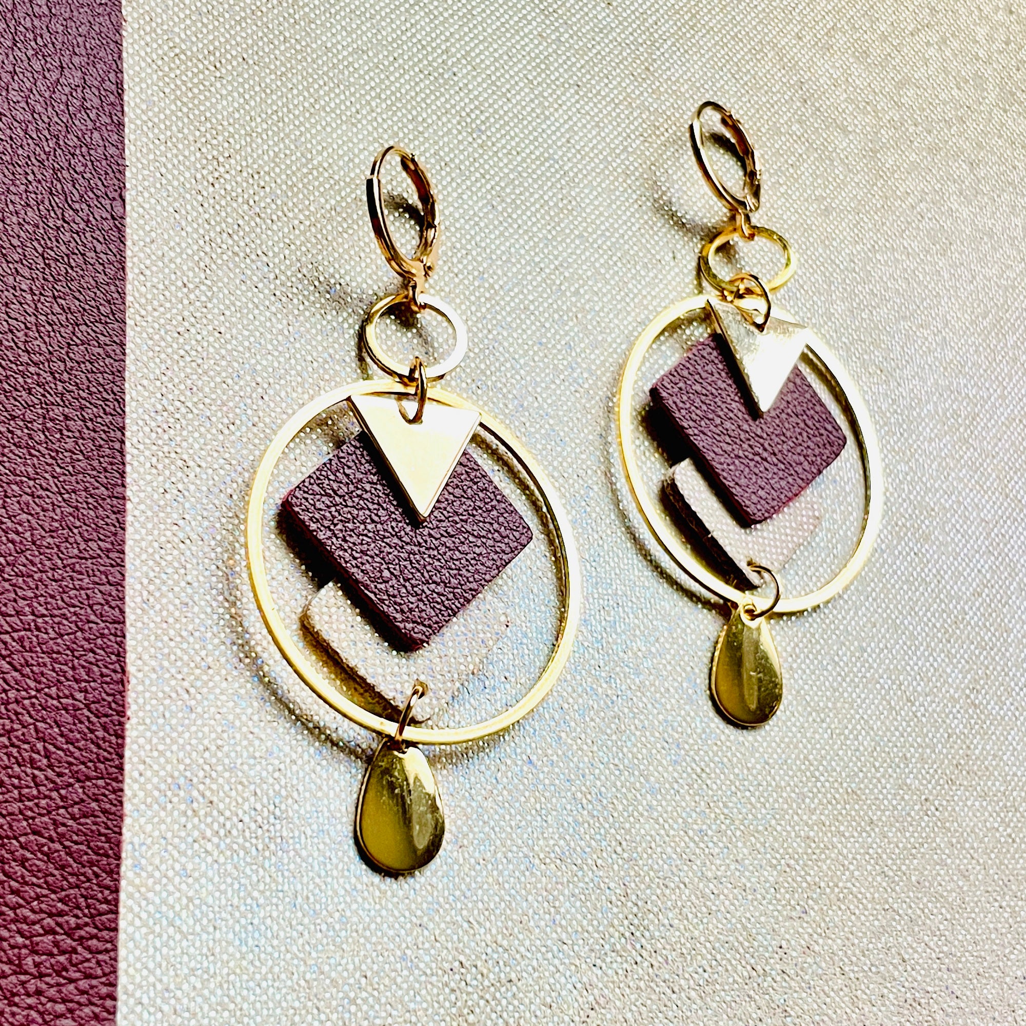 Boucles d'oreilles Nune modèle Créoles Adamante Or en cuir grenat grainé et laiton doré à l'or fin sur fond beige irisé