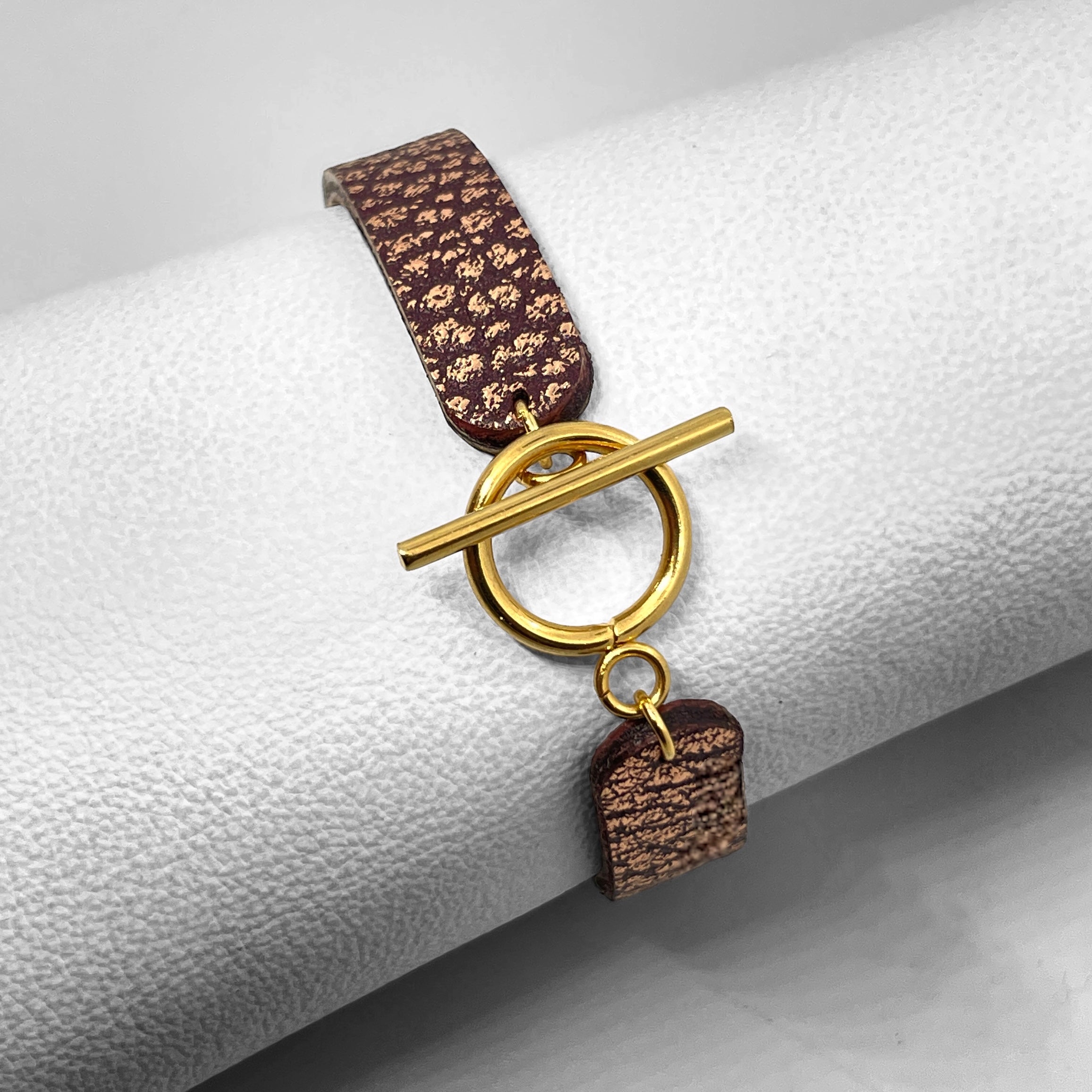 Bracelet en cuir chocolat grainé or rose vu de dessous avec fermoir en T doré, enroulé autour d'un rouleau de cuir blanc