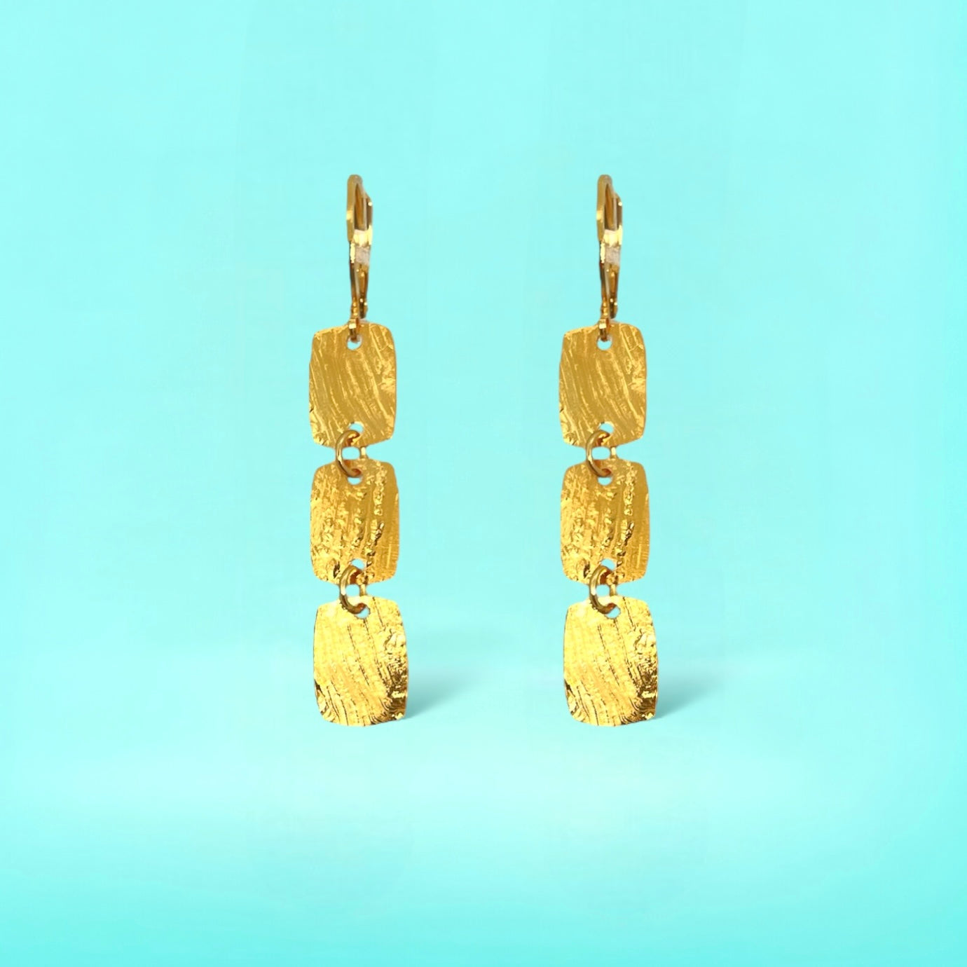 Fines boucles d'oreilles dorées pendantes en chapelet de 3 petits rectangles, sur fond bleu