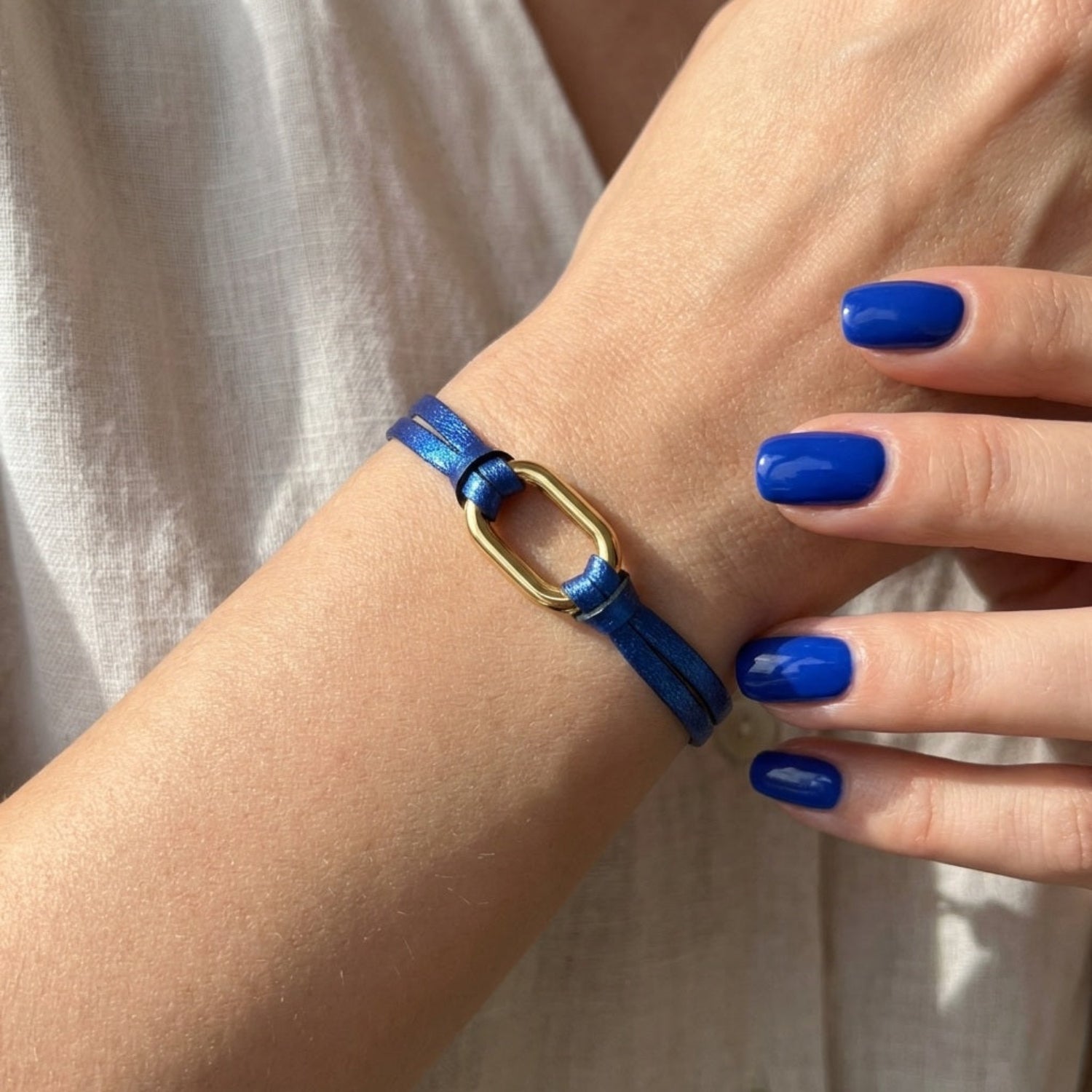 Bracelet à boucle dorée en fins liens de cuir bleu cobalt métallisé, porté au pognet