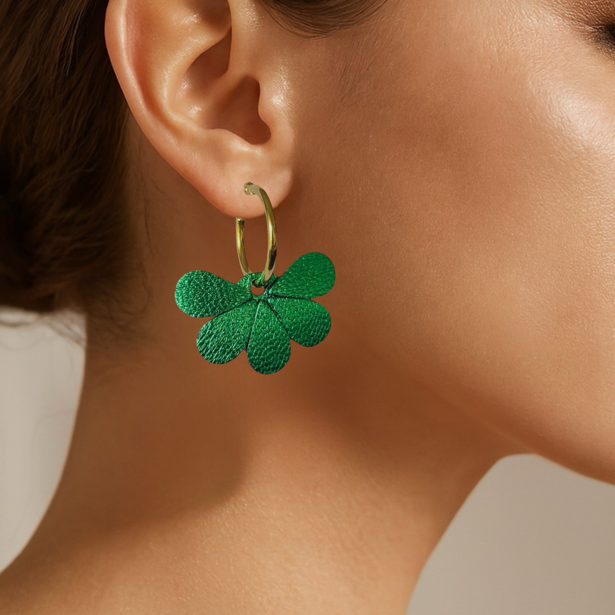 Boucles d'oreilles créoles dorées avec pendentifs en cuir vert métallisé en forme de fleurs, portées à l'oreille