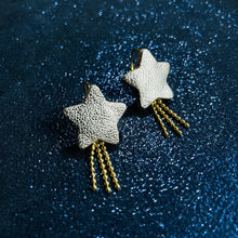 Charger l&#39;image dans la galerie, boucles d&#39;oreilles dorées Nune modèle Stella en forme d&#39;étoiles, en cuir argent, sur fond noir paillettes
