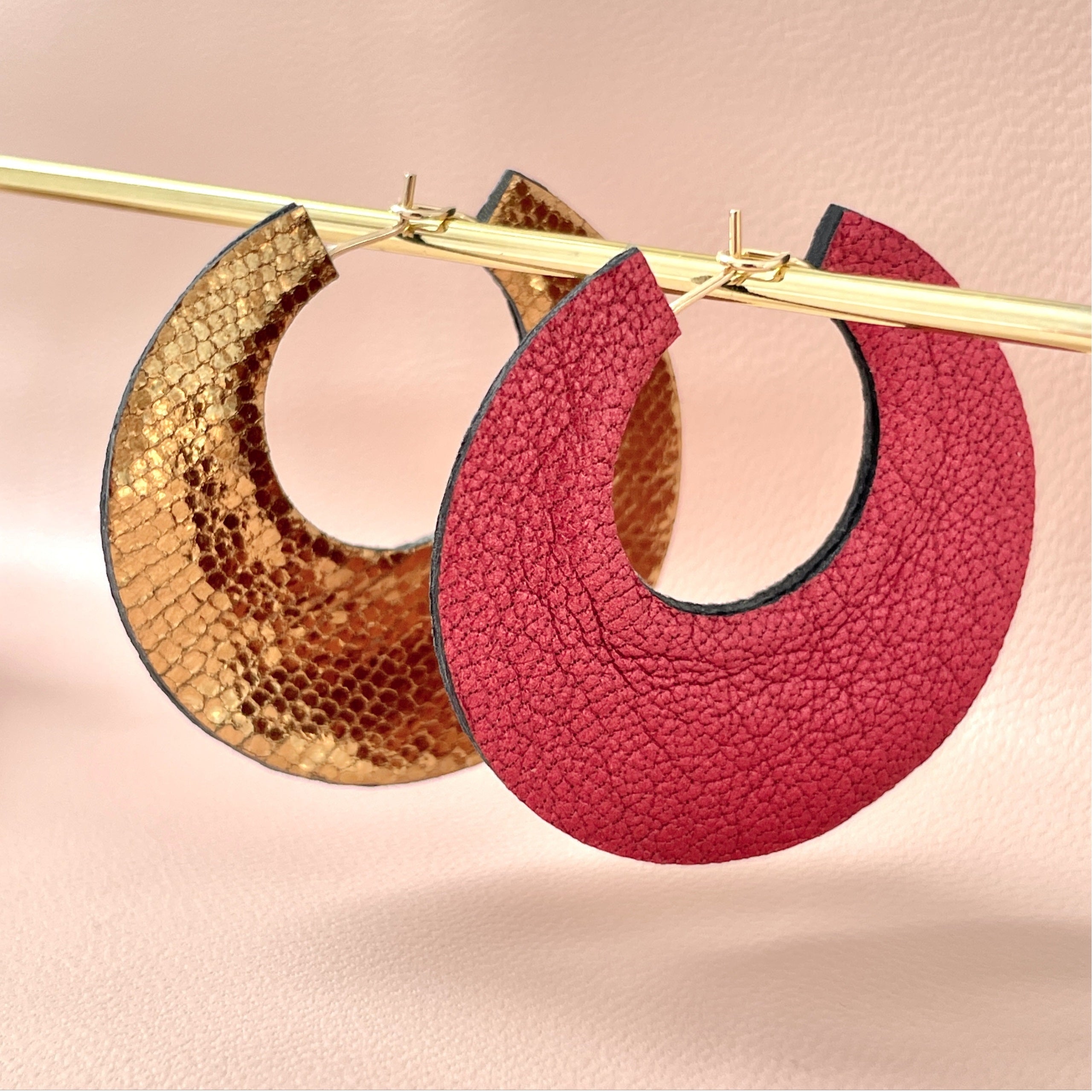 NUNE grandes boucles d'oreilles créoles dorées rondes tout-cuir Circus, un côté rubis métallisé, l'autre côté bronze brillant façon serpent, pendues sur un portant doré