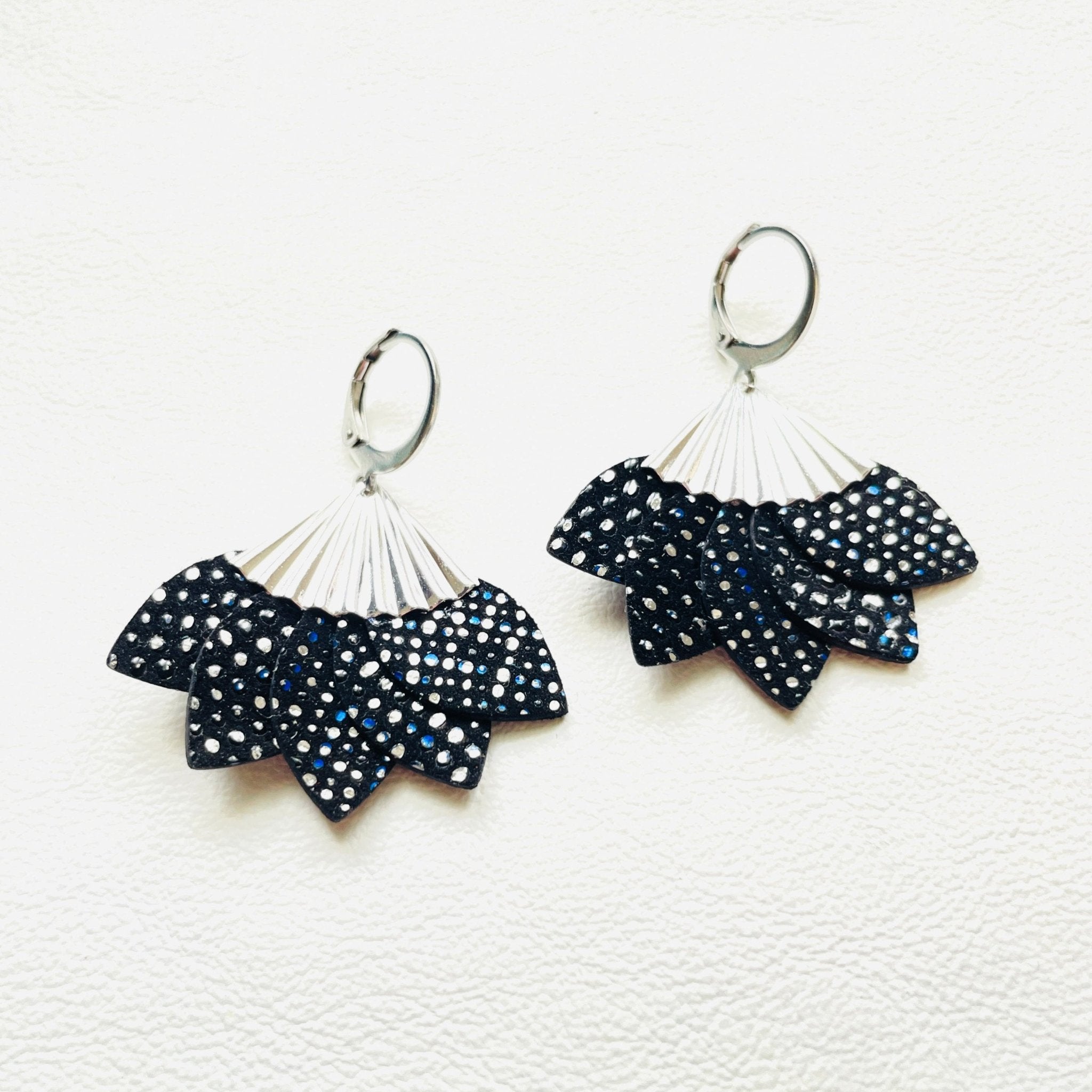 Boucles d'oreilles argentées Nune modèle Sakura en pétales de cuir noir à pois argent, sur fond cuir blanc