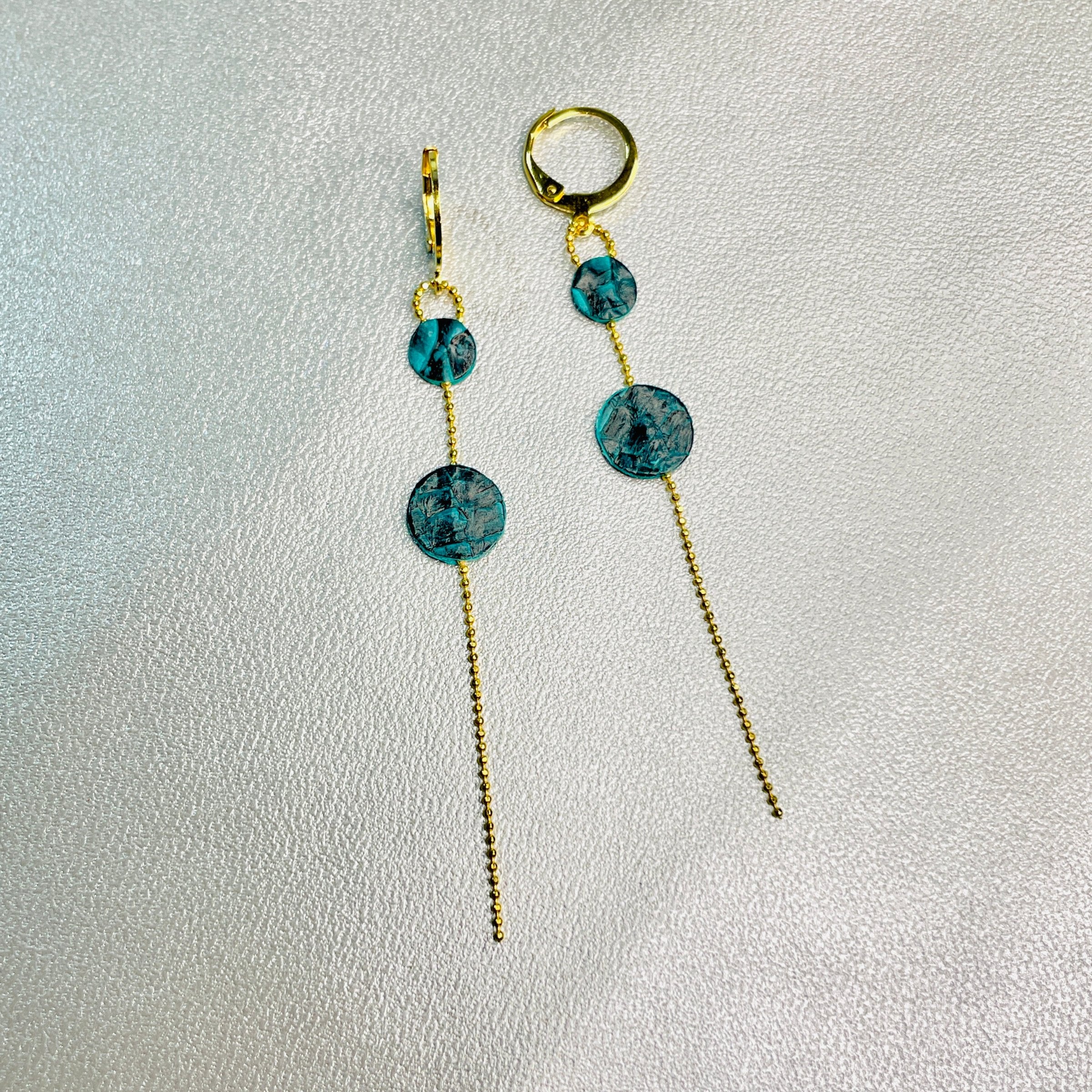 Fines boucles d'oreilles Lyre de Nune, dorées à l'or fin avec petites pastilles de cuir marin, cuir de poisson saumon vert émeraude écaille sur chaînette dorée, sur fond gris argenté