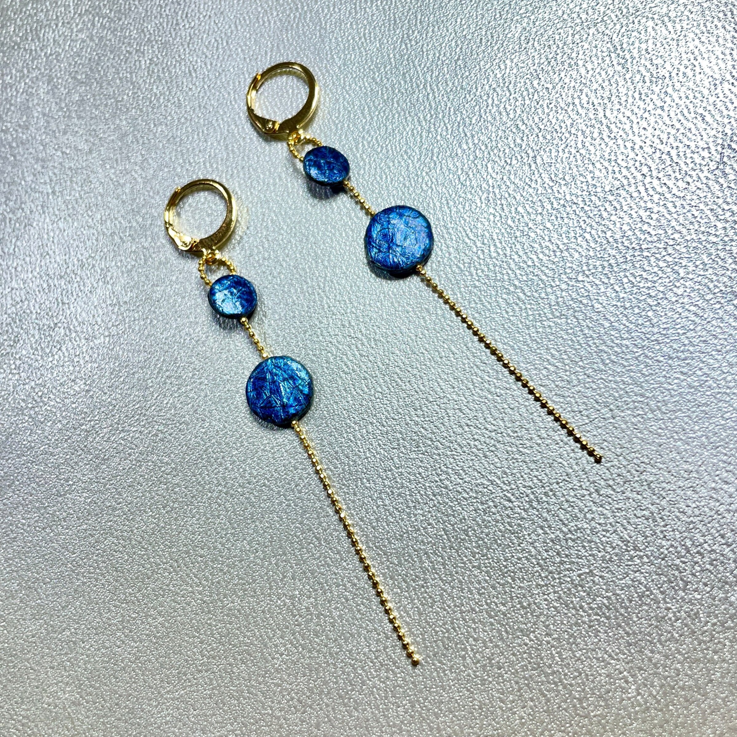 Fines boucles d'oreilles Lyre de Nune, dorées à l'or fin avec petites pastilles de cuir marin, cuir de poisson saumon bleu saphir métallisé sur chaînette dorée, sur fond gris argenté