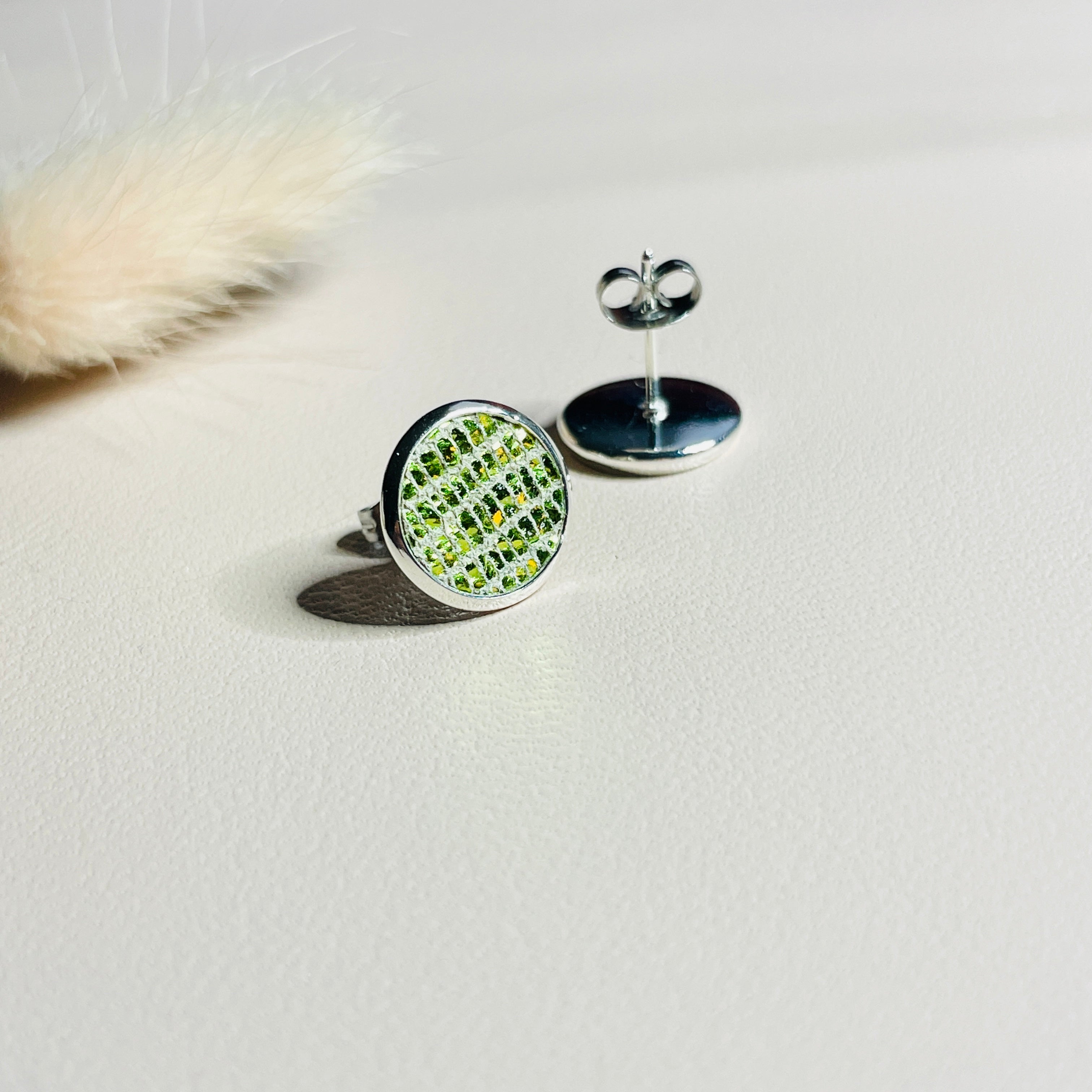 Puces d'oreilles argentées rondes Nune modèle Ilis argenté avec pastilles de cuir vert olive métallisé, sur fond de cuir blanc cassé