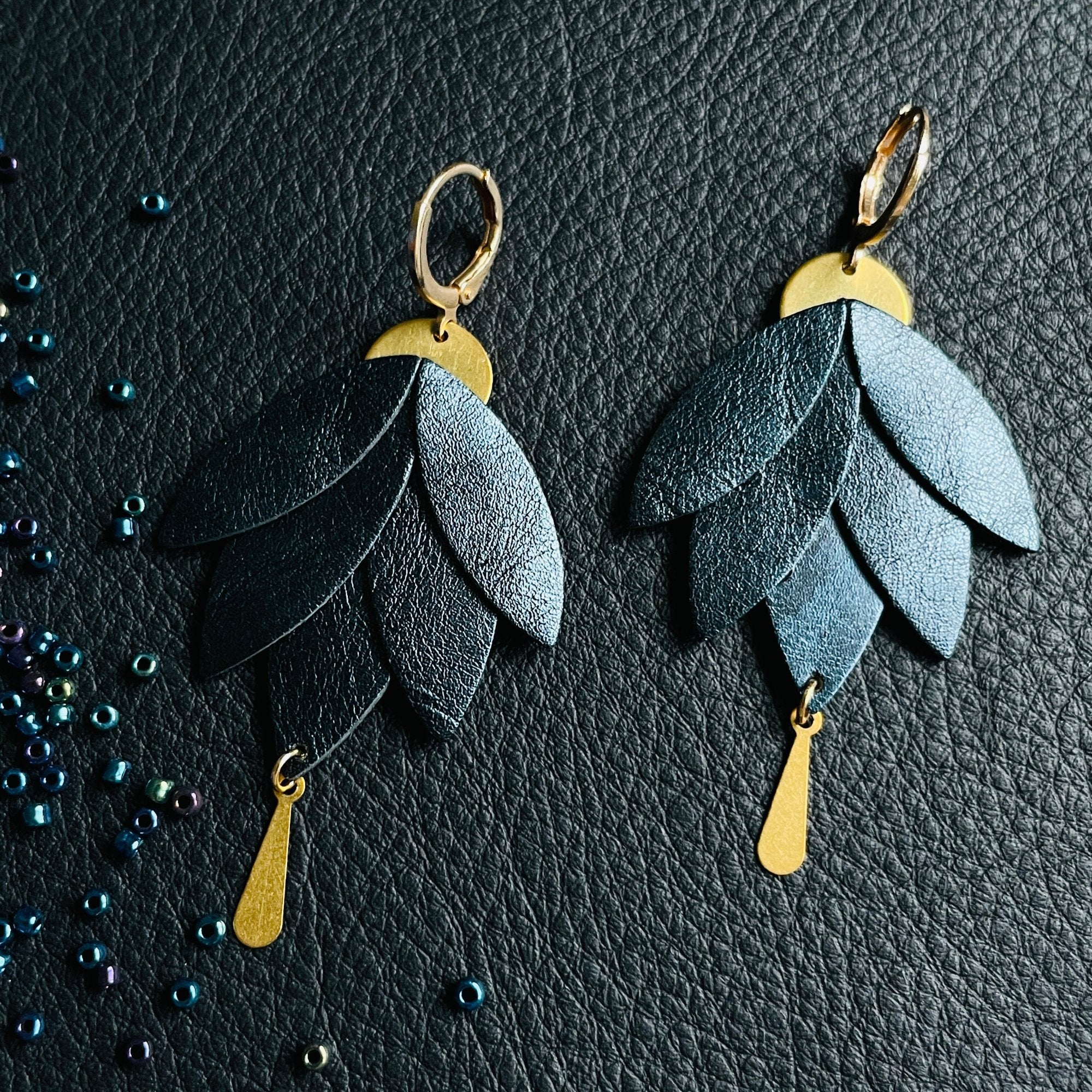 Boucles d'oreilles dorées pendantes Nune modèle Nymphéa en cuir bleu nuit métallisé, sur fond de cuir noir grainé et perles de rocaille