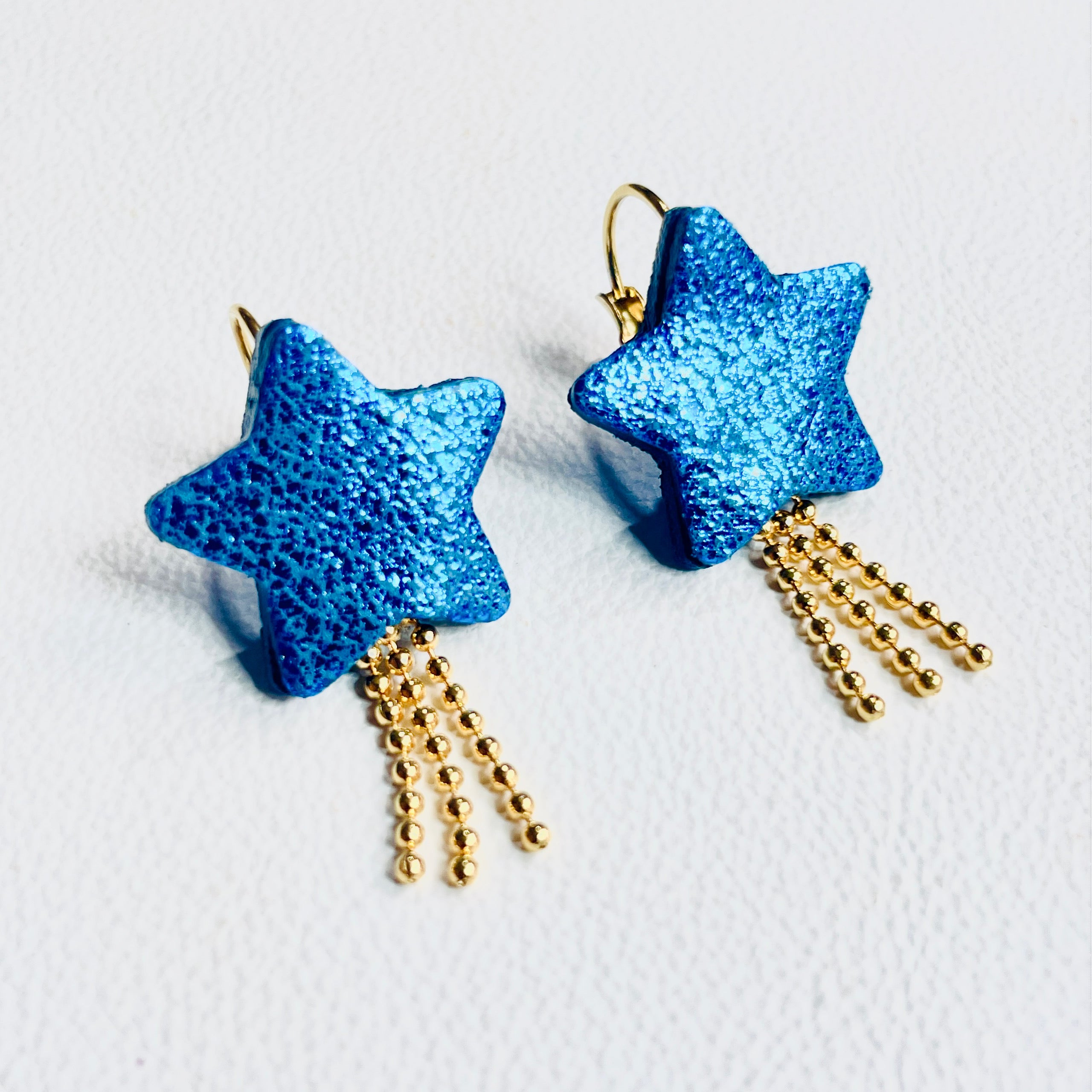 boucles d'oreilles dorées Nune modèle Stella en forme d'étoiles, en cuir bleu roi métallisé, sur fond blanc