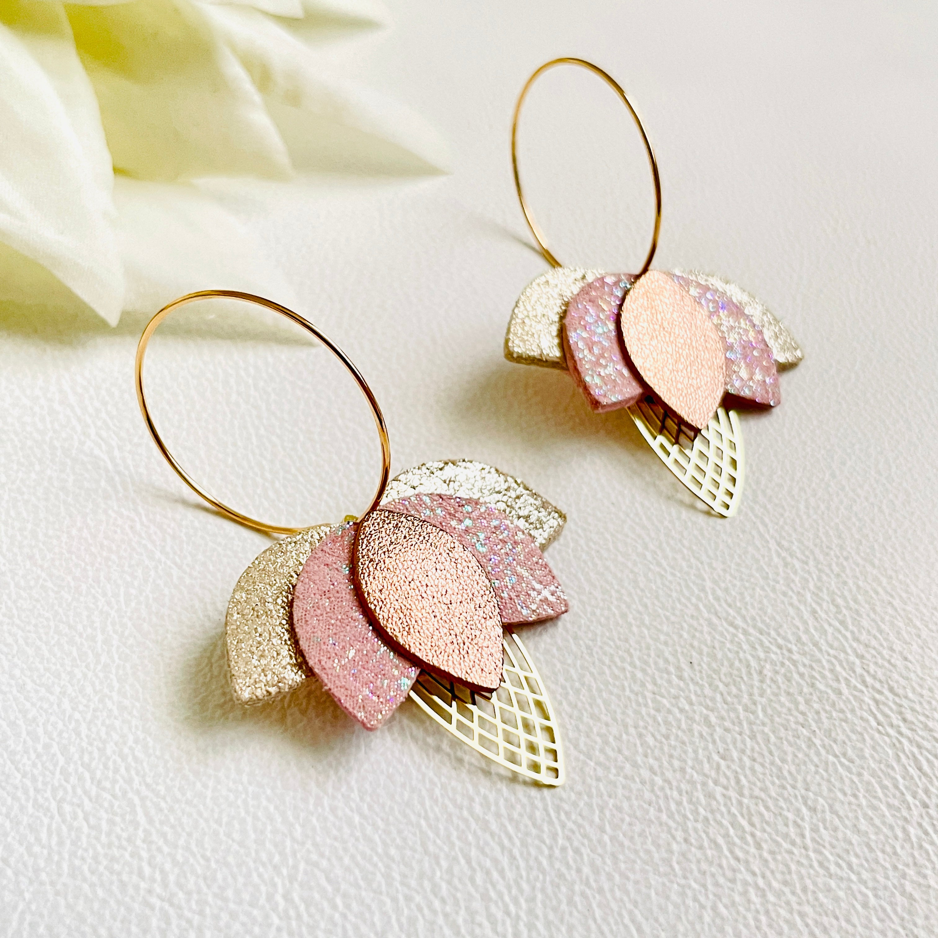 Créoles dorées en forme de fleurs de Lotus en cuirs beige pailleté argent, rose pâle irisé et cannelle dorée satinée sur fond blanc