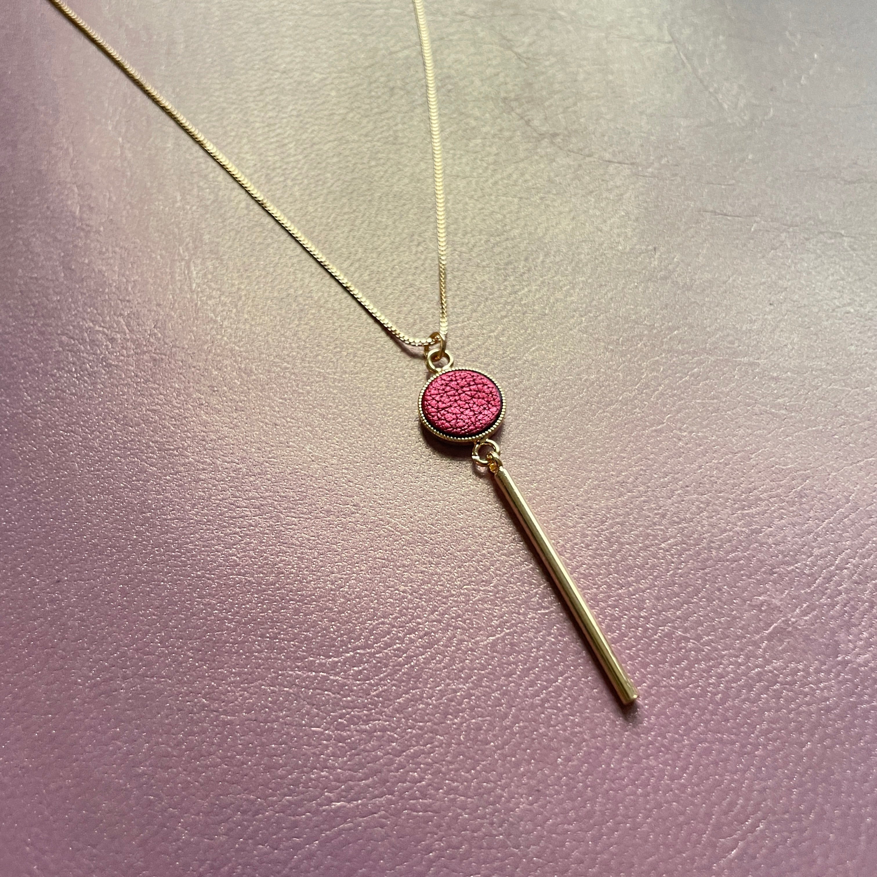 Nune fin collier doré Nida et pendentif effilé avec pastille de cuir rubis métallisé, sur fond cuir mauve irisé