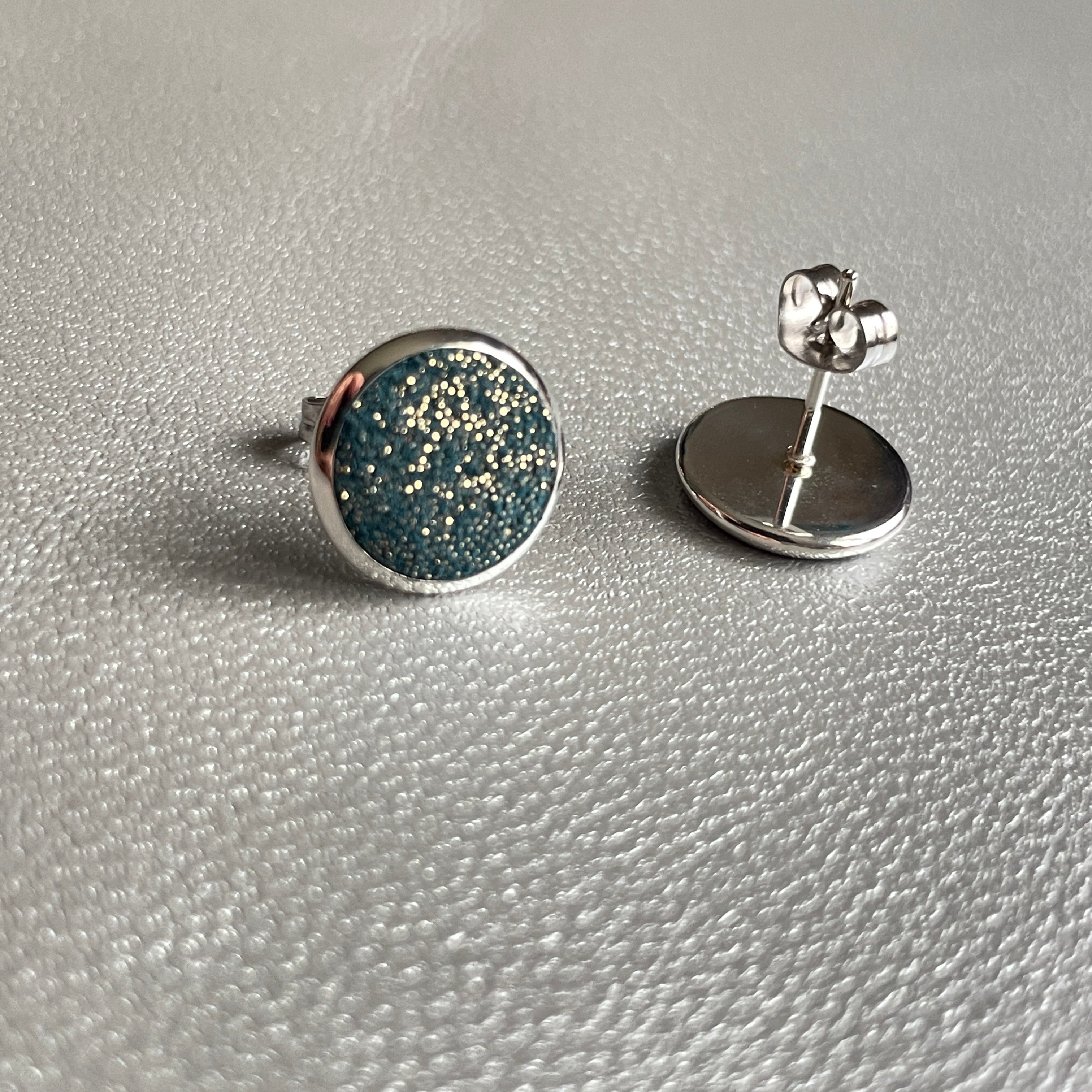 Puces d'oreilles argentées rondes Nune modèle Ilis argenté pailleté avec pastilles de cuir vert canard pailleté or, sur fond de cuir gris métallisé